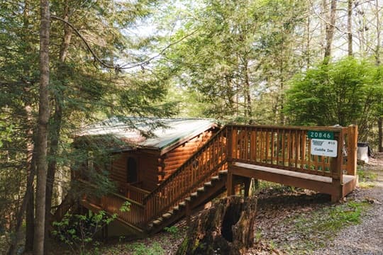 A wooden cabin nestled in a forest, featuring a staircase and a green sign indicating "Cuddle Inn."
