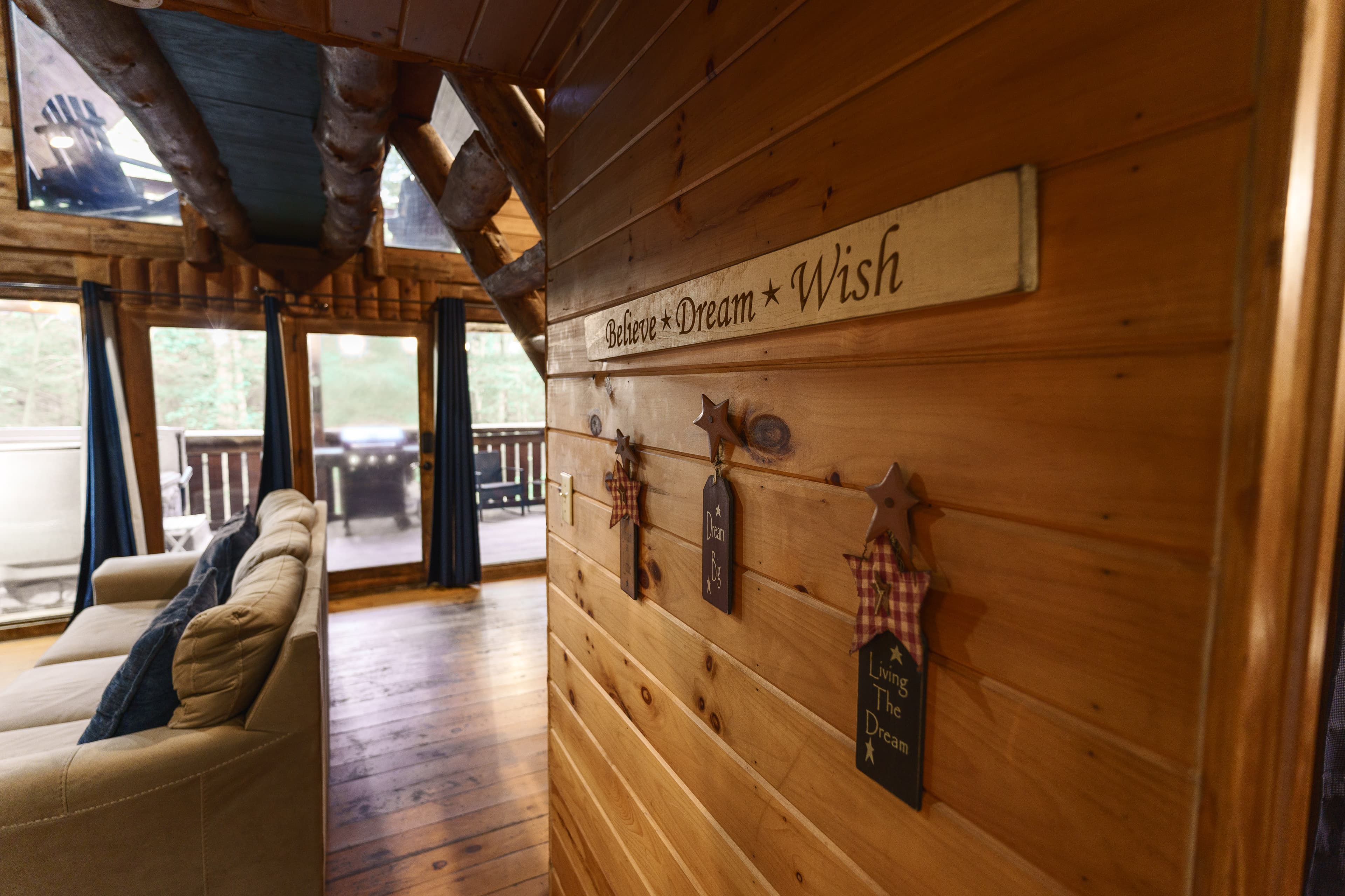 Interior of a cozy wooden cabin featuring a wall with inspirational signs and a view of the outdoor deck.
