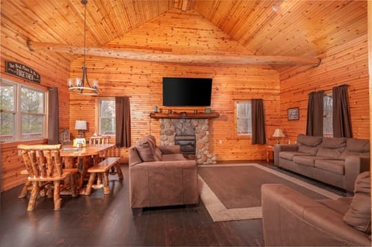 Cozy wooden cabin interior featuring a stone fireplace, dining area, and comfortable seating.