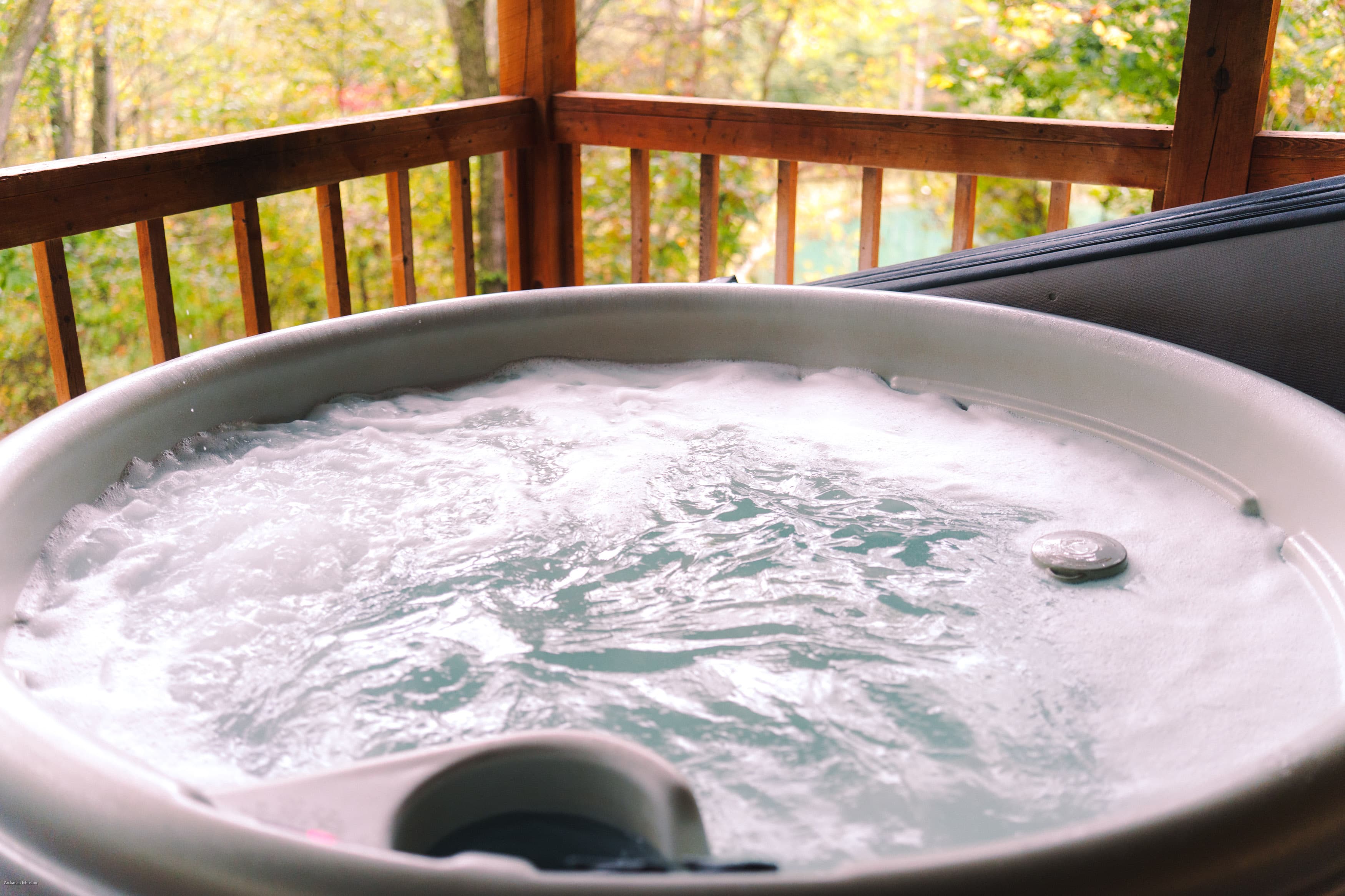 A bubbling hot tub on a wooden deck surrounded by autumn foliage.