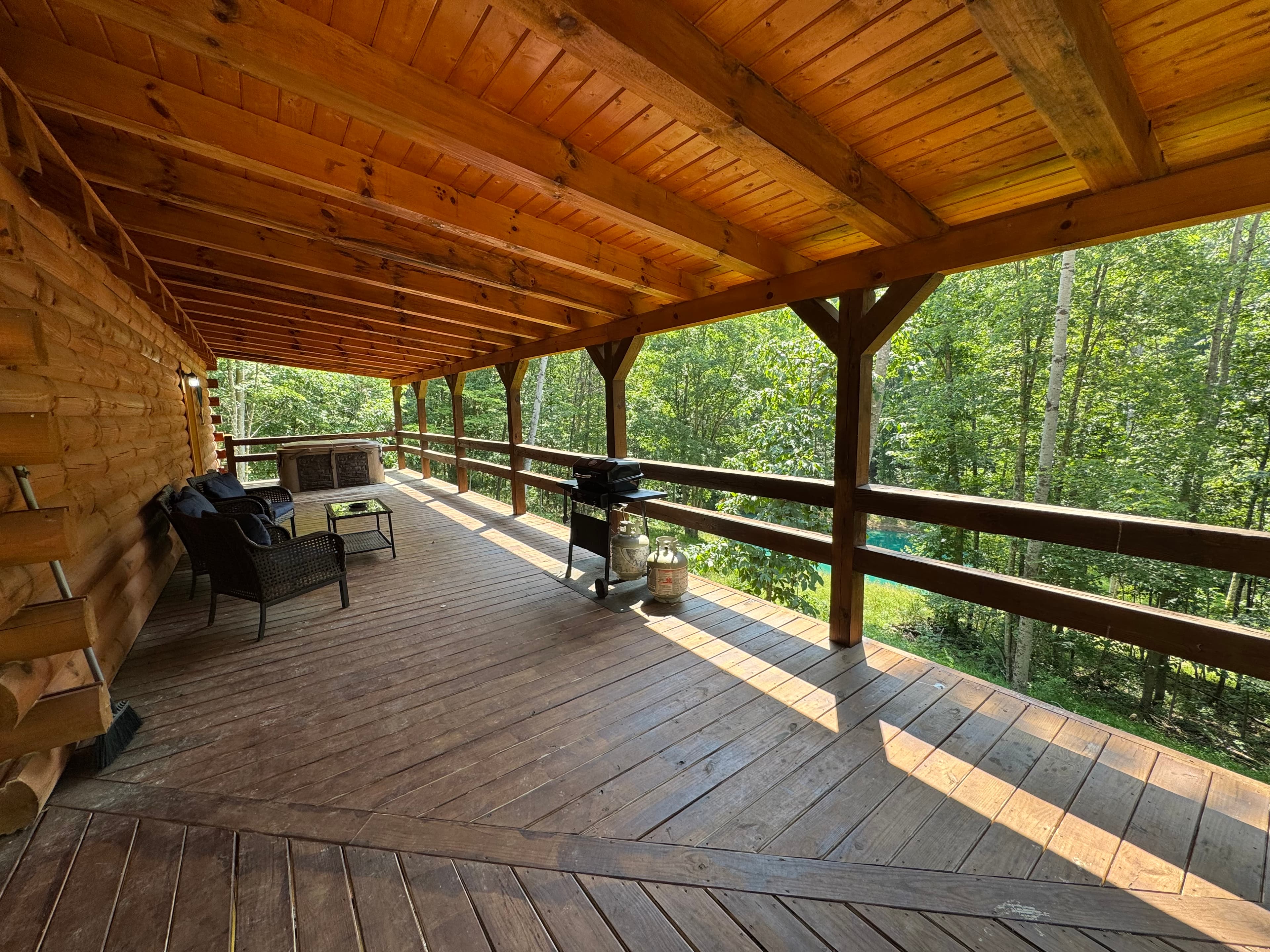 A wooden porch with a grill and seating area overlooking a green forest.