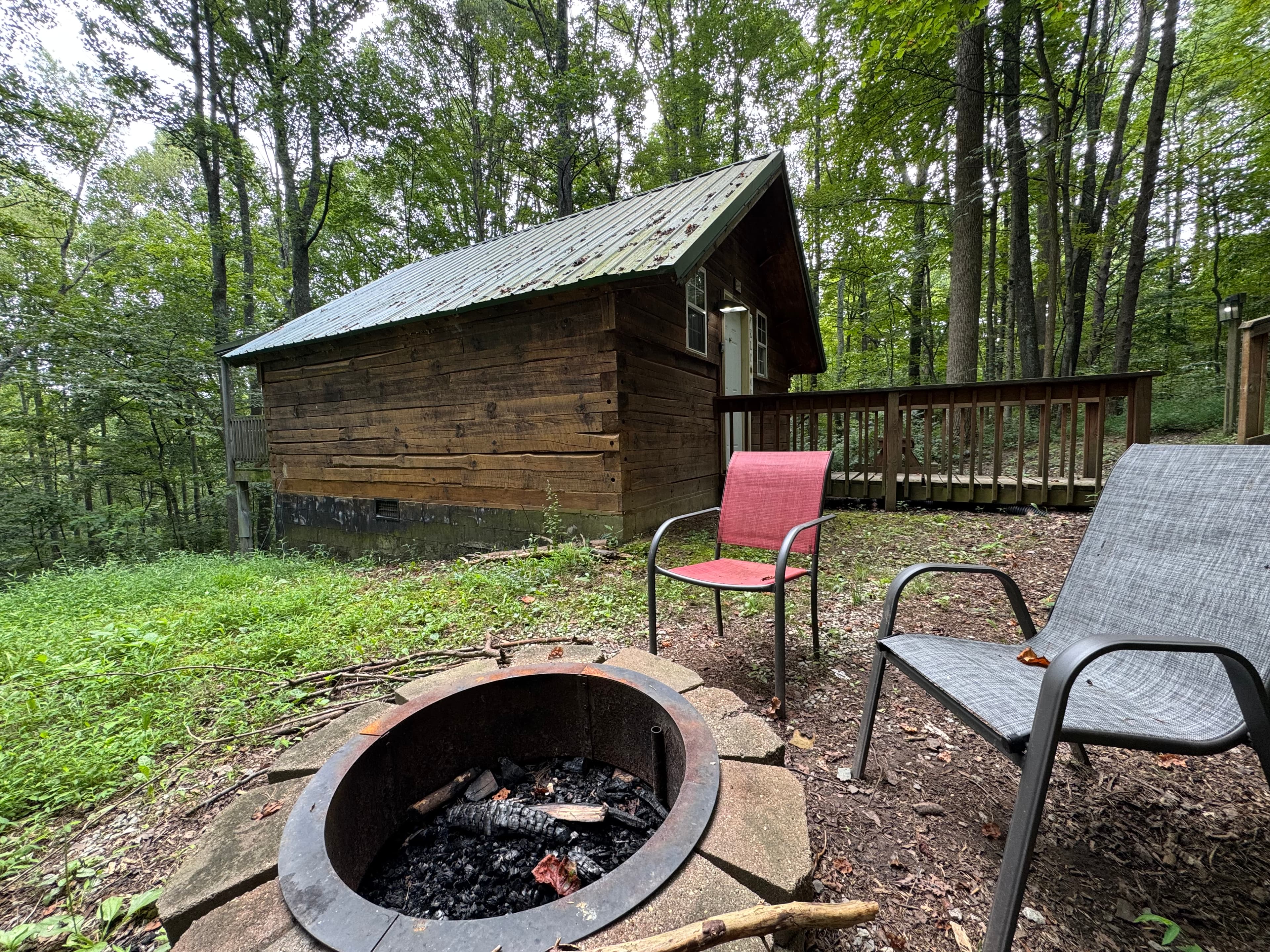 A cozy cabin in the woods with two chairs next to a fire pit.