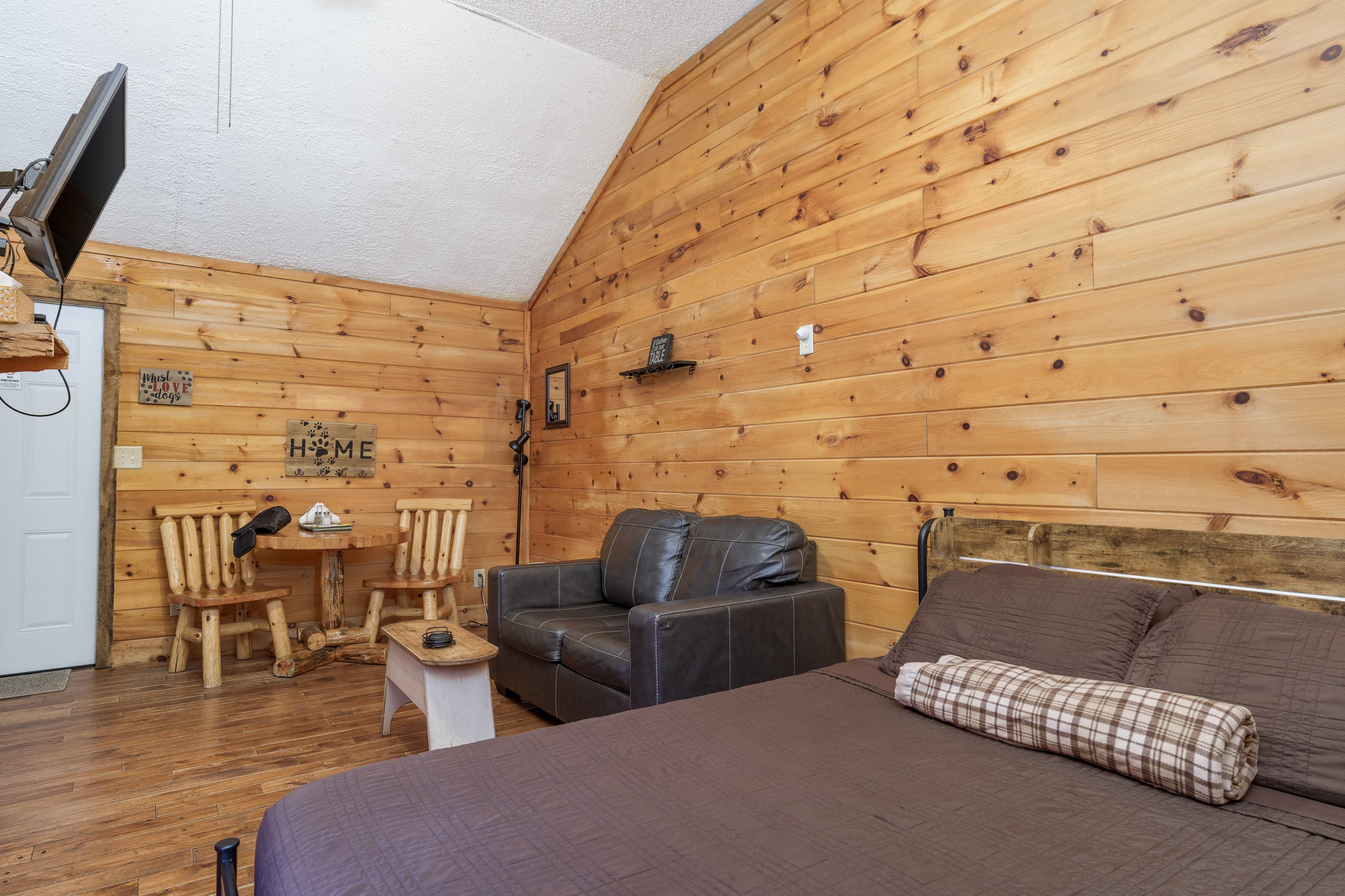 Cozy cabin interior with wooden walls, a bed, a sofa, and a small dining area.