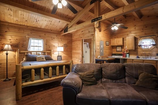 Interior of a rustic cabin featuring a wooden bed, leather sofa, and kitchen area.