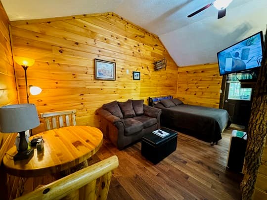 Cozy cabin interior featuring wood-paneled walls, a couch, a bed, and a small dining table.