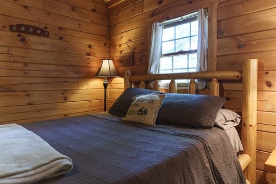 Cozy wooden bedroom with a bed, lamp, and window.