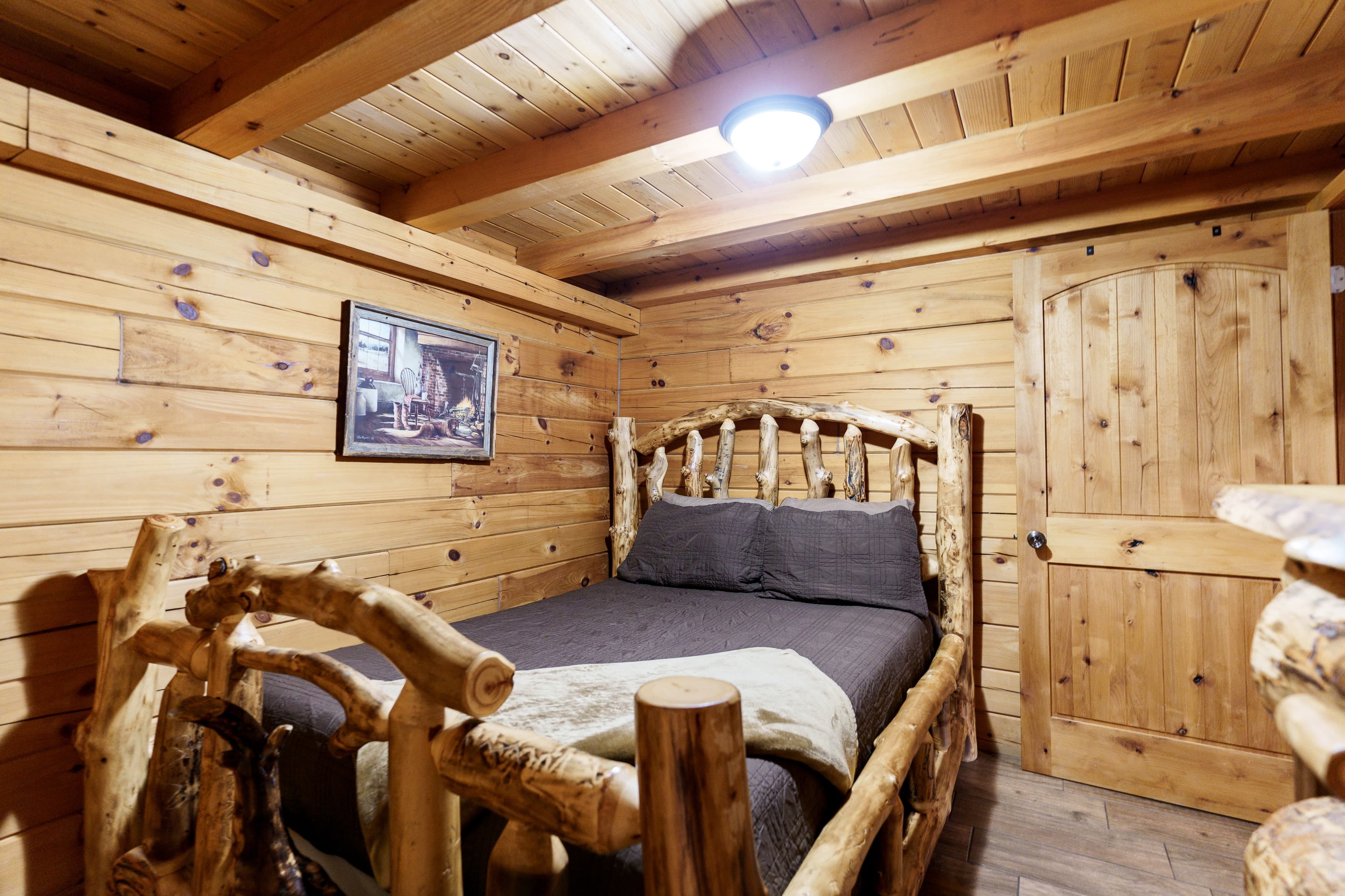 A cozy log cabin bedroom featuring a wooden bed, warm wood paneling, and a door.