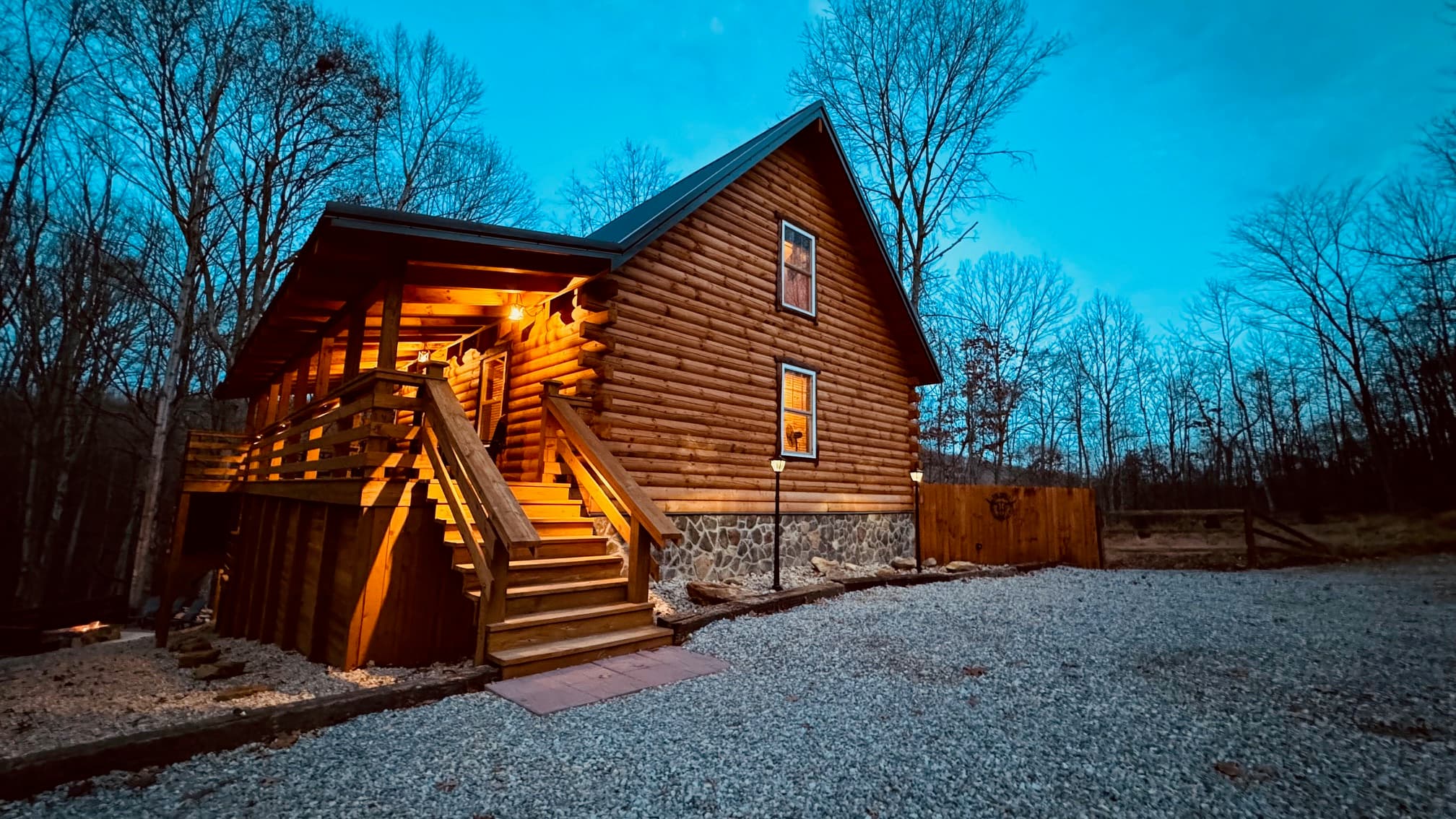 A warm lit log cabin surrounded by trees at twilight.