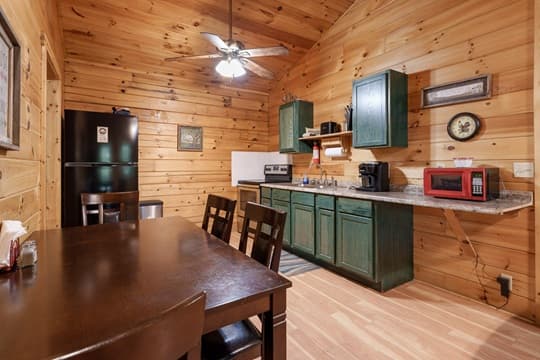 A cozy wooden kitchen featuring a dining table, green cabinets, and various appliances.