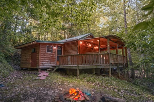 A cozy wooden cabin nestled in a forest, with a deck and a fire pit in front.