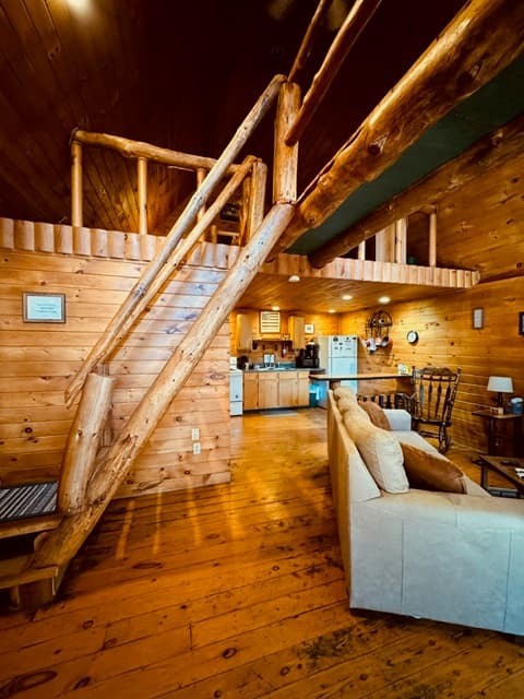 Cozy wooden interior of a cabin featuring a staircase, living area, and kitchen.