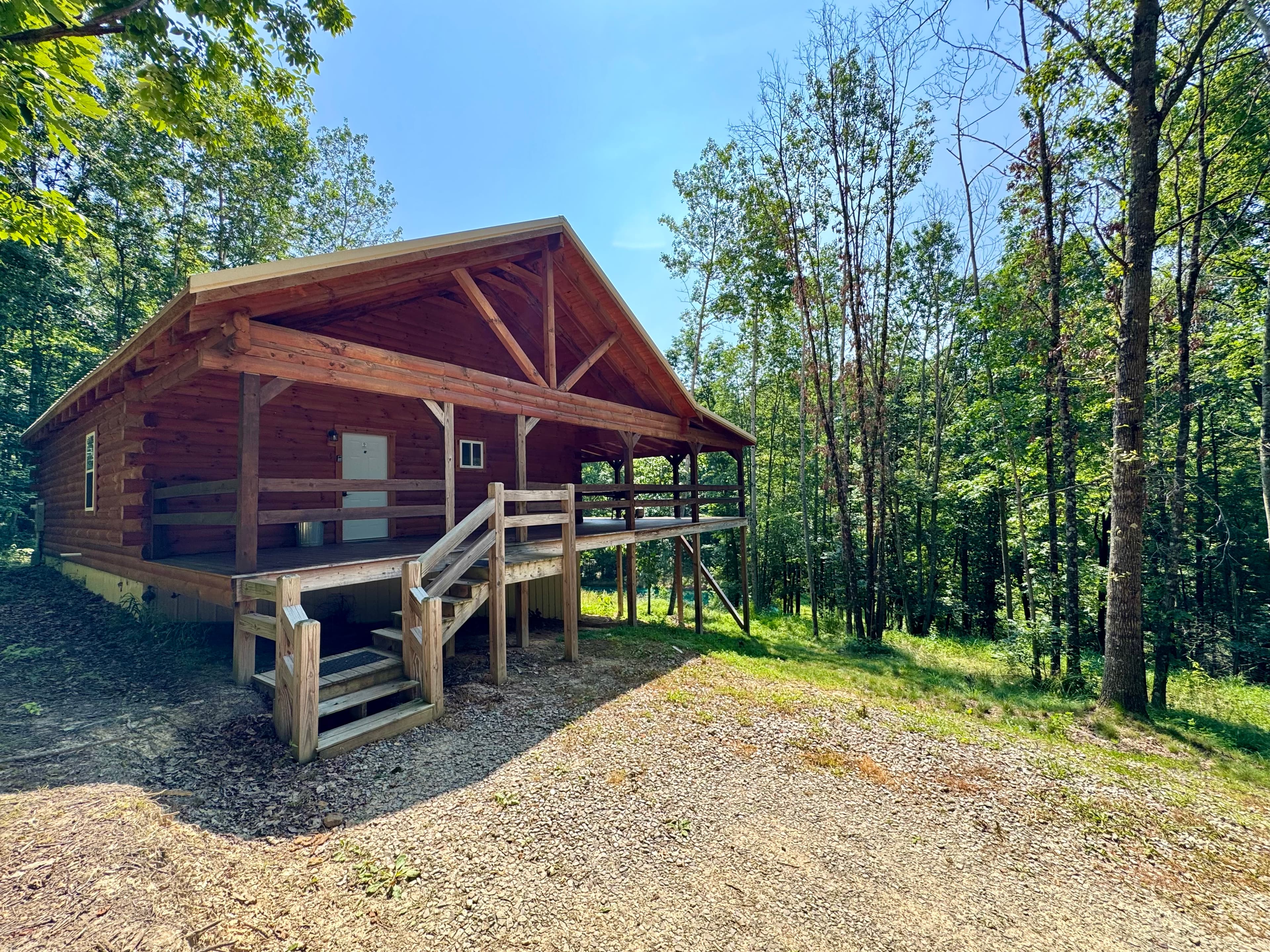 A wooden cabin with a large porch surrounded by trees.