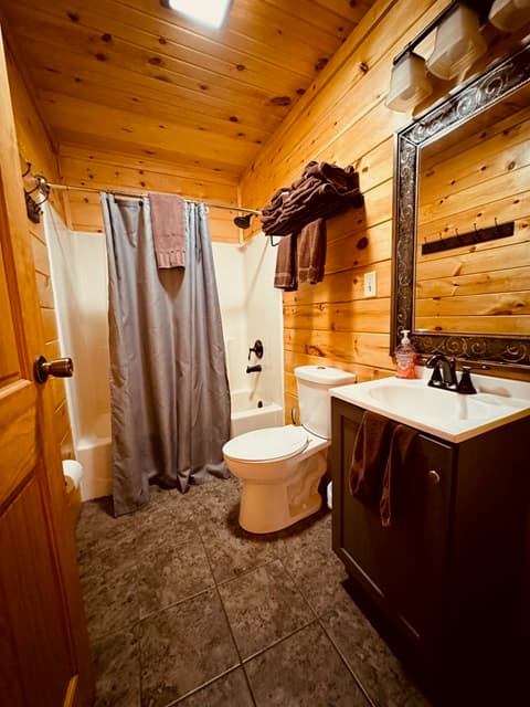 A rustic bathroom featuring wooden walls, a shower with a gray curtain, a sink with a dark cabinet, and a toilet.