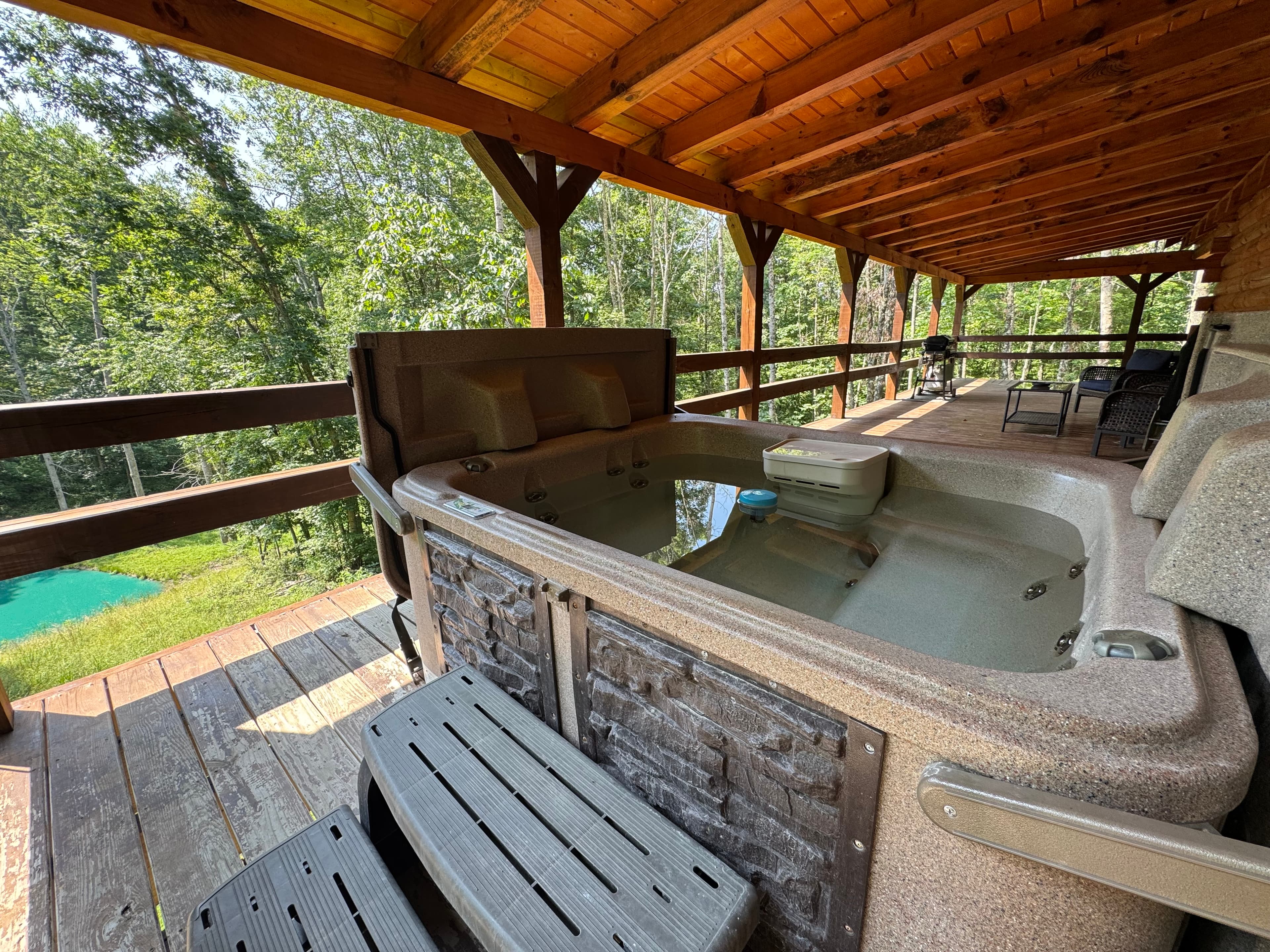 A hot tub sits on a wooden deck surrounded by trees.