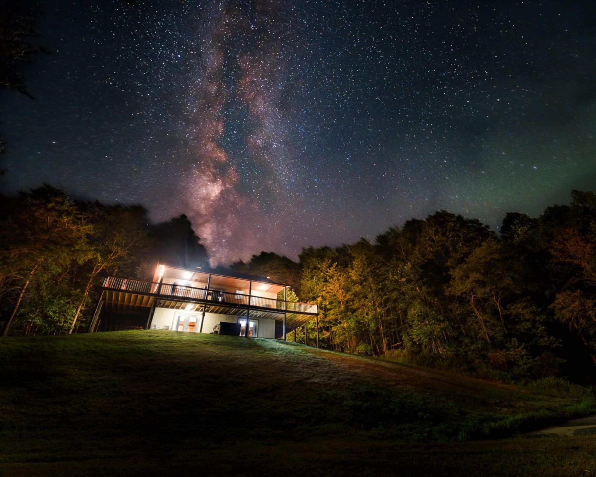 A modern house on a hillside under a starry night sky, with the Milky Way visible.