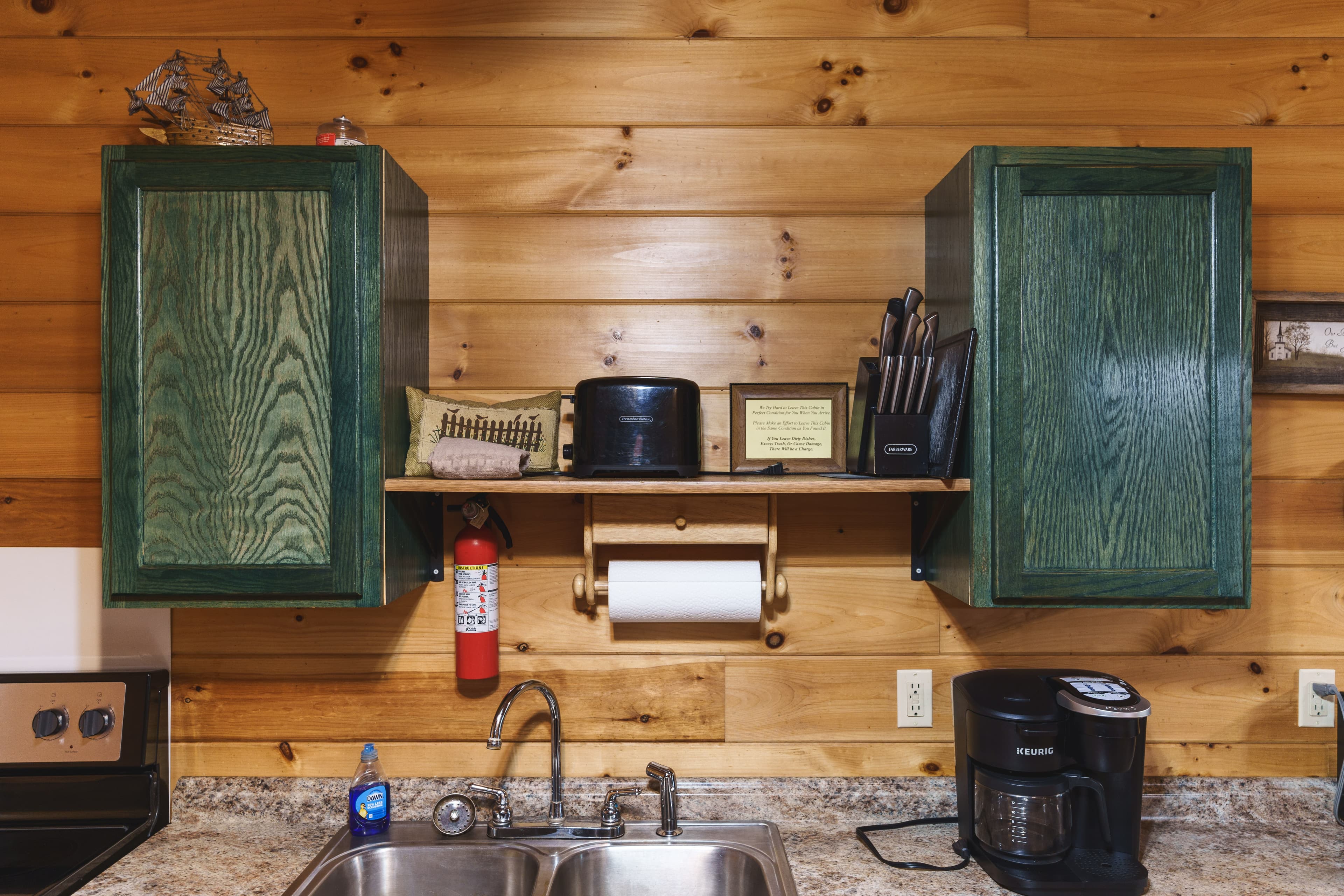 A rustic kitchen with green cabinets, a sink, coffee maker, and various utensils on display.