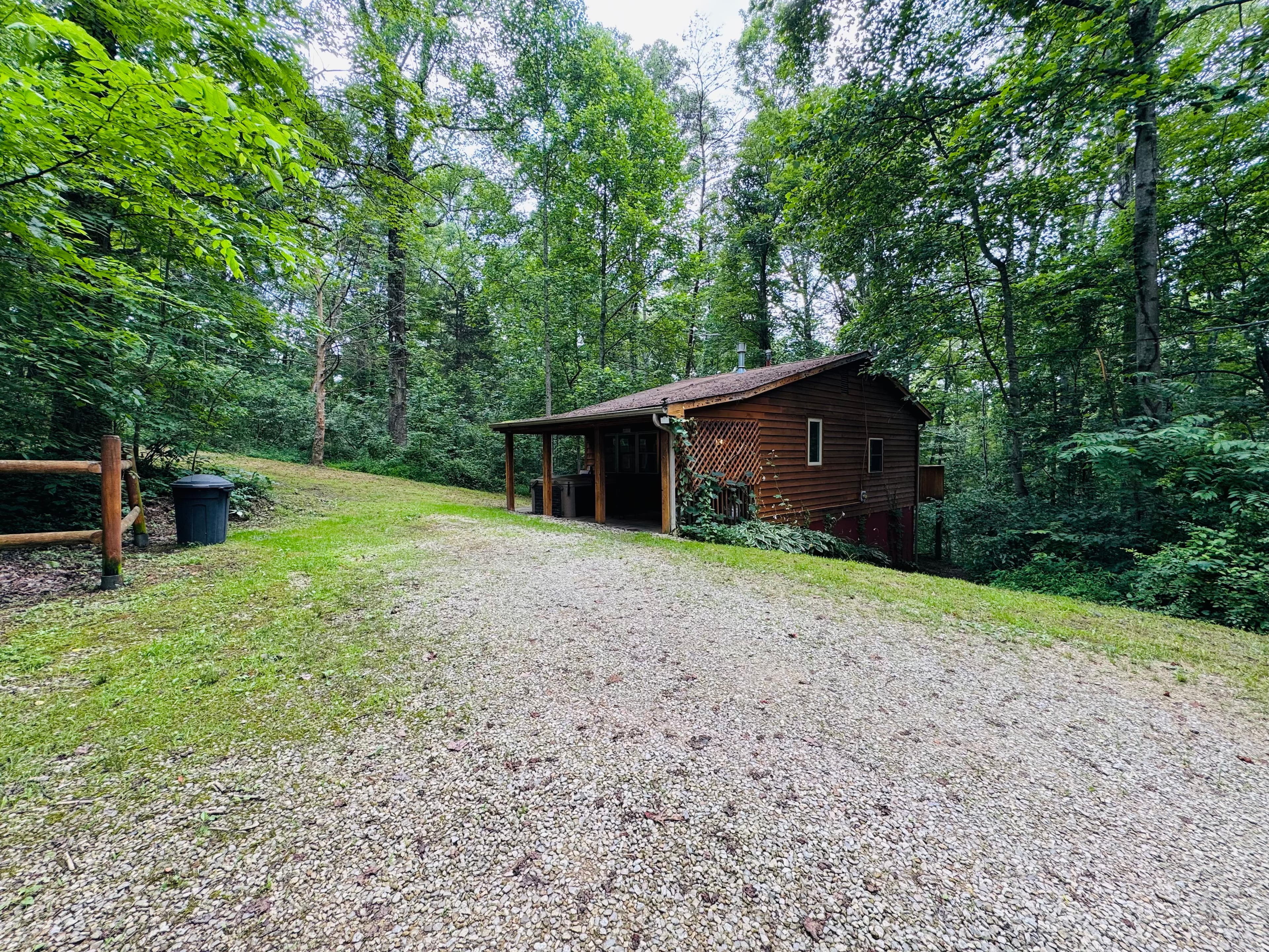 A gravel driveway leads to a wooden cabin surrounded by dense greenery.