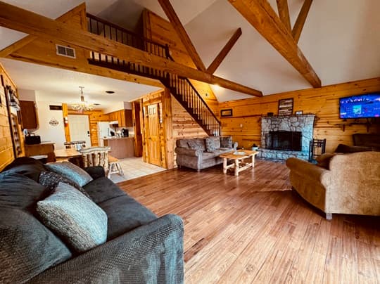 A cozy, wooden interior living room featuring a staircase, stone fireplace, and comfortable seating.