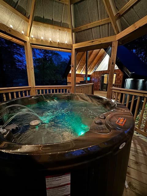 A hot tub with glowing water inside a wooden gazebo at night.