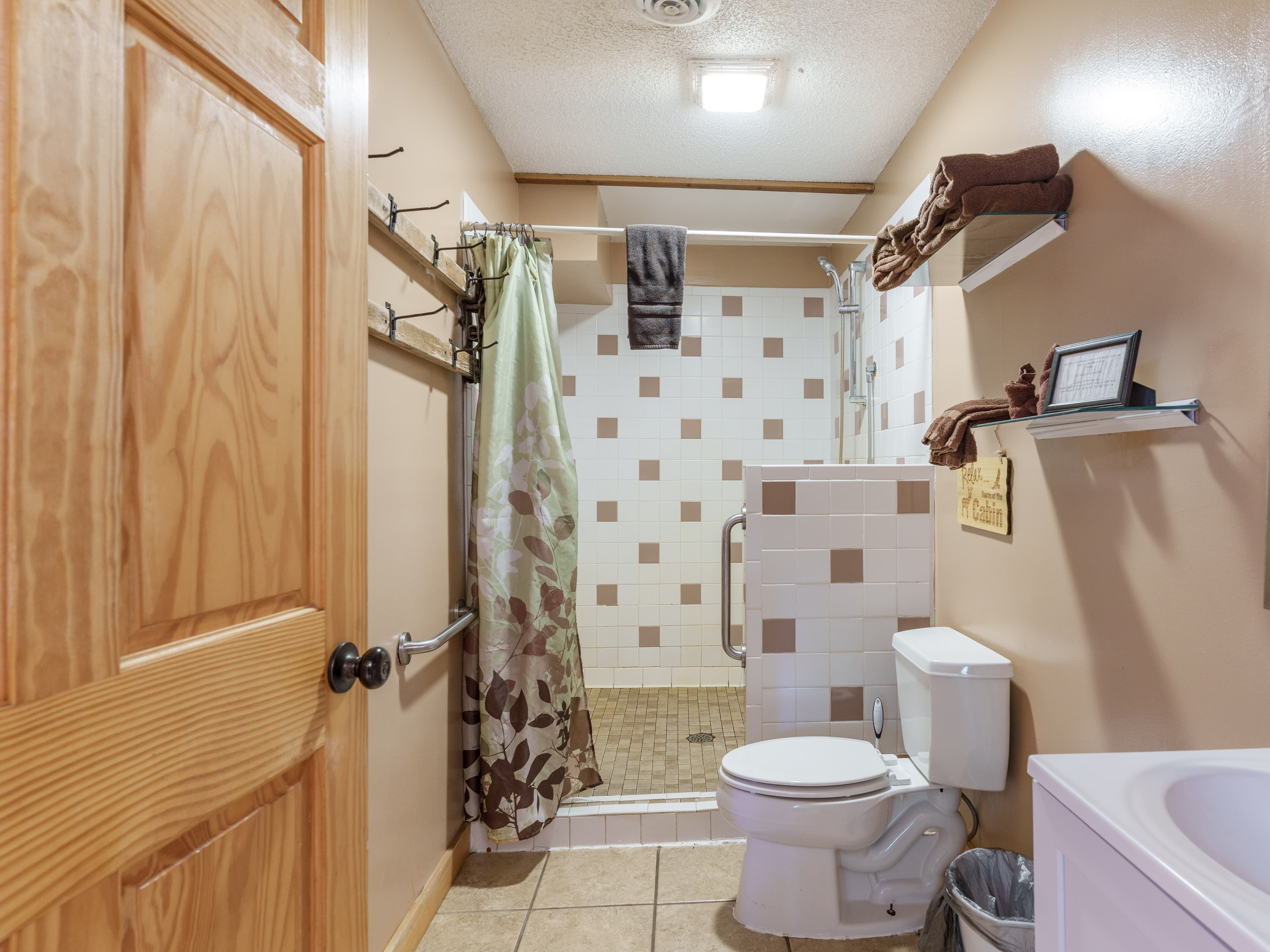 A well-lit bathroom featuring a shower, toilet, and tiled walls with a mix of brown and cream tones.