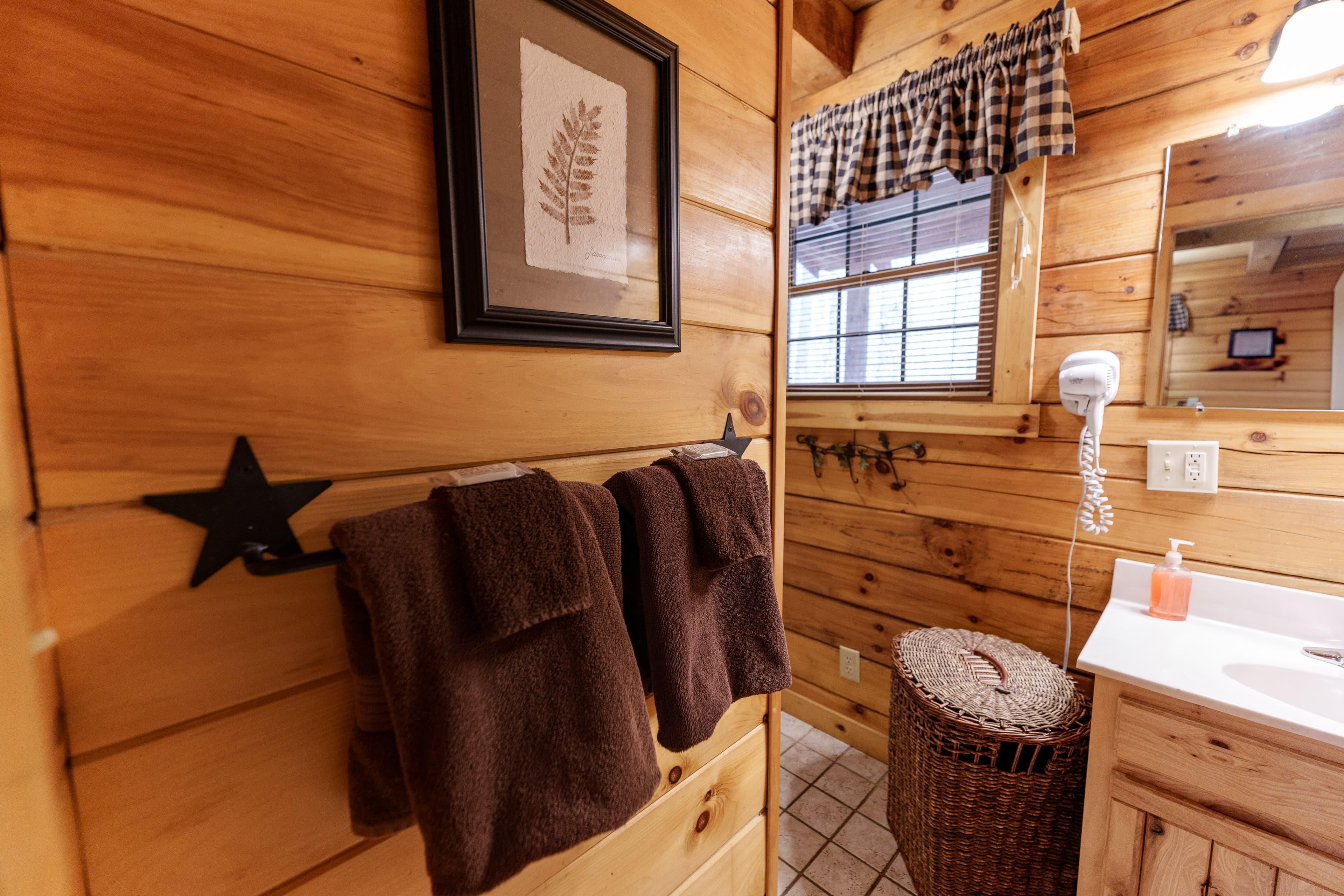 A rustic bathroom featuring wooden walls, brown towels, and a wicker laundry basket.