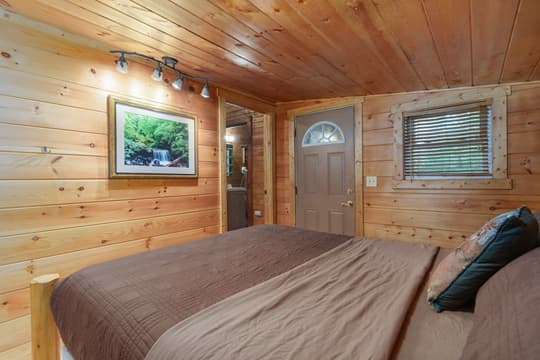 A cozy wooden-paneled bedroom featuring a bed, a door, and a nature-themed artwork.