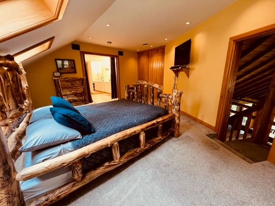 A cozy attic bedroom featuring a rustic wooden bed, blue pillows, and warm yellow walls.