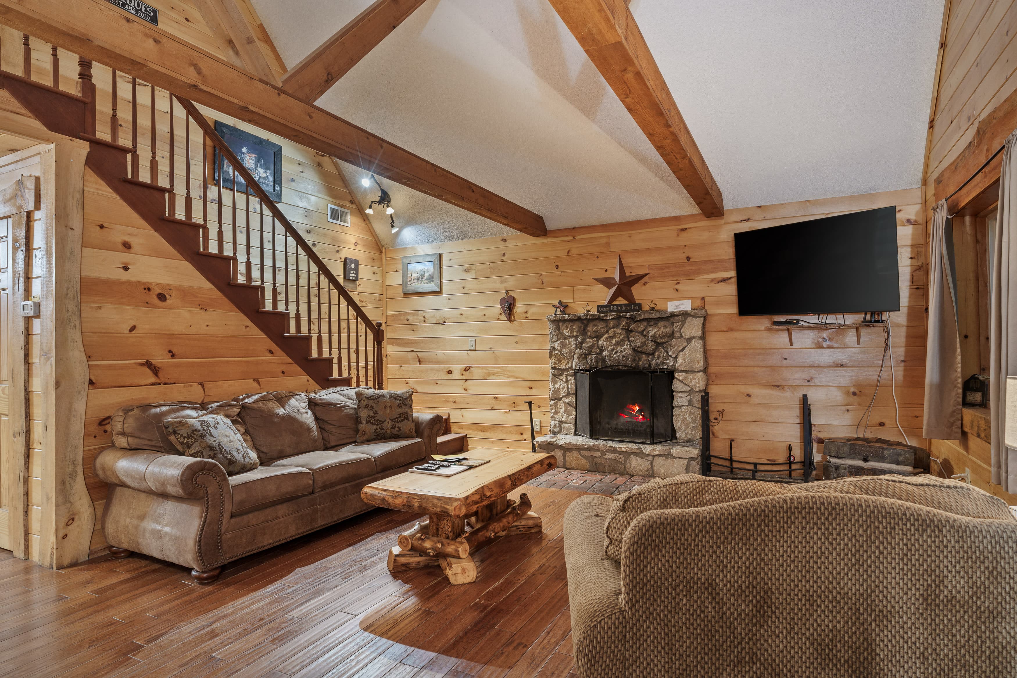 Cozy living room featuring wooden walls, a stone fireplace, a flat-screen TV, and comfortable seating.