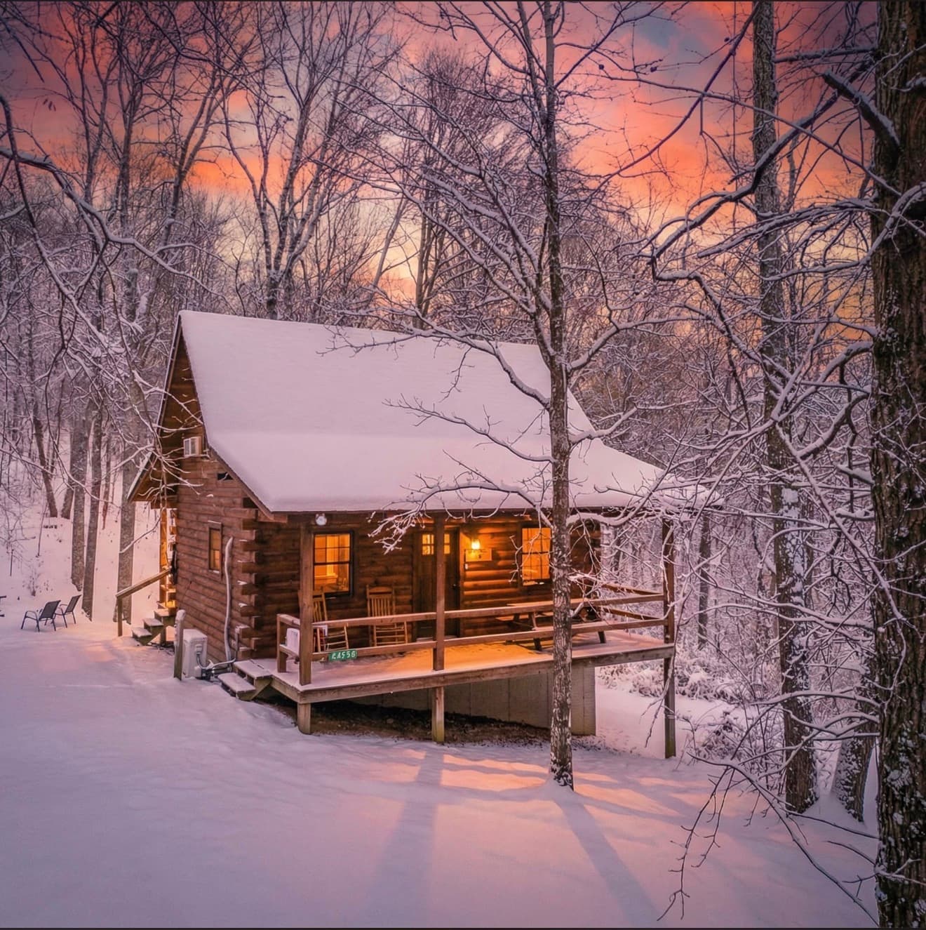 A cozy log cabin nestled in a snowy landscape at sunset.