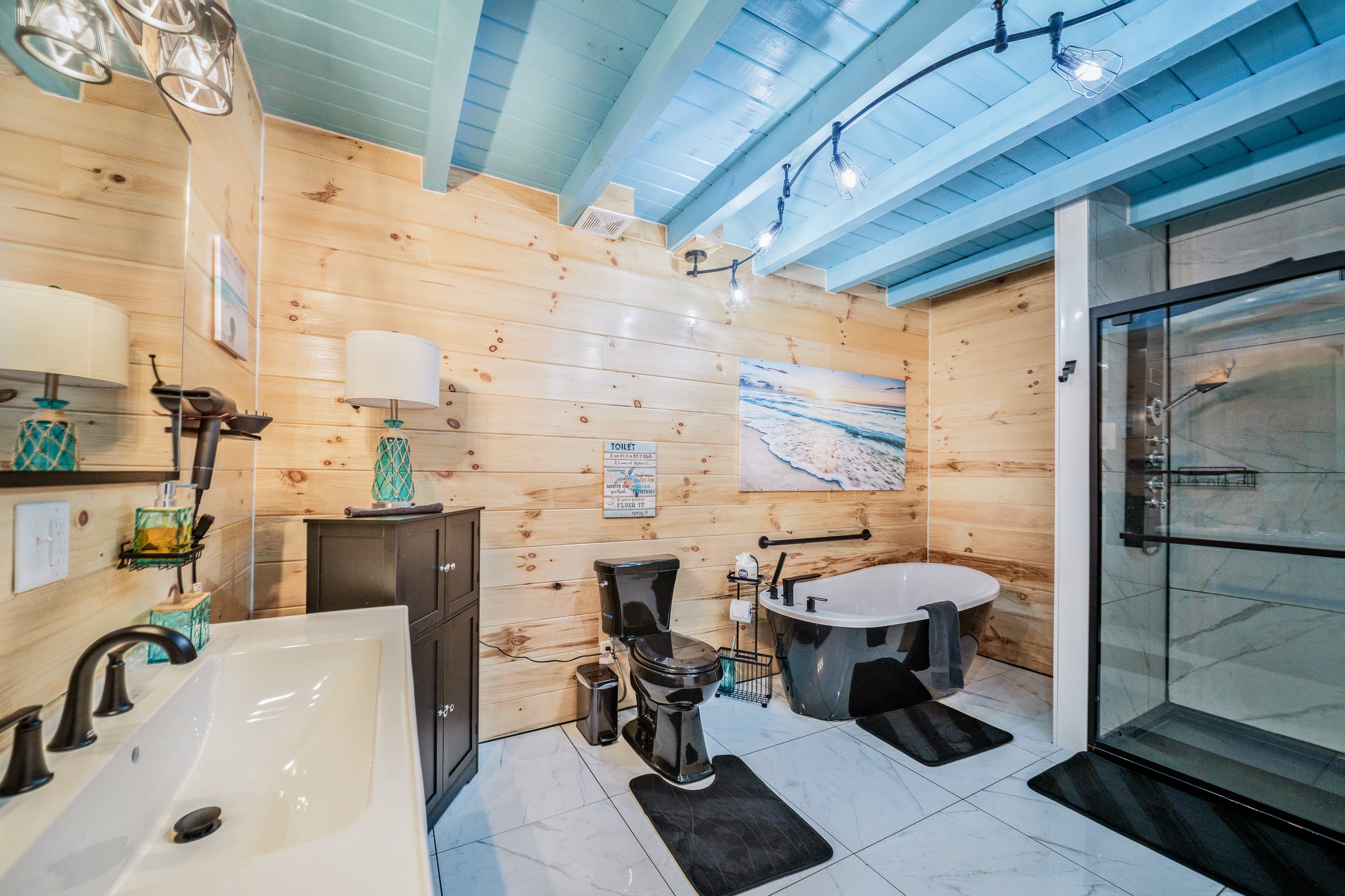 Modern bathroom featuring wooden walls, blue beams, a freestanding tub, and a glass shower.