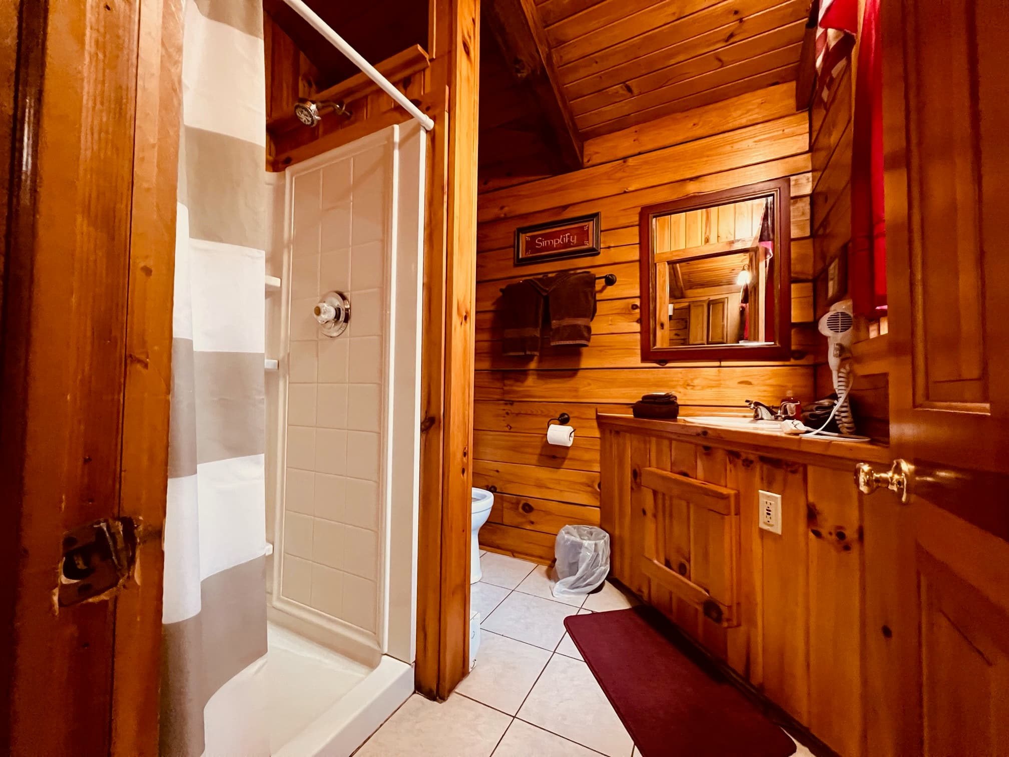 A rustic bathroom featuring a shower, wooden walls, and a vanity with a mirror.