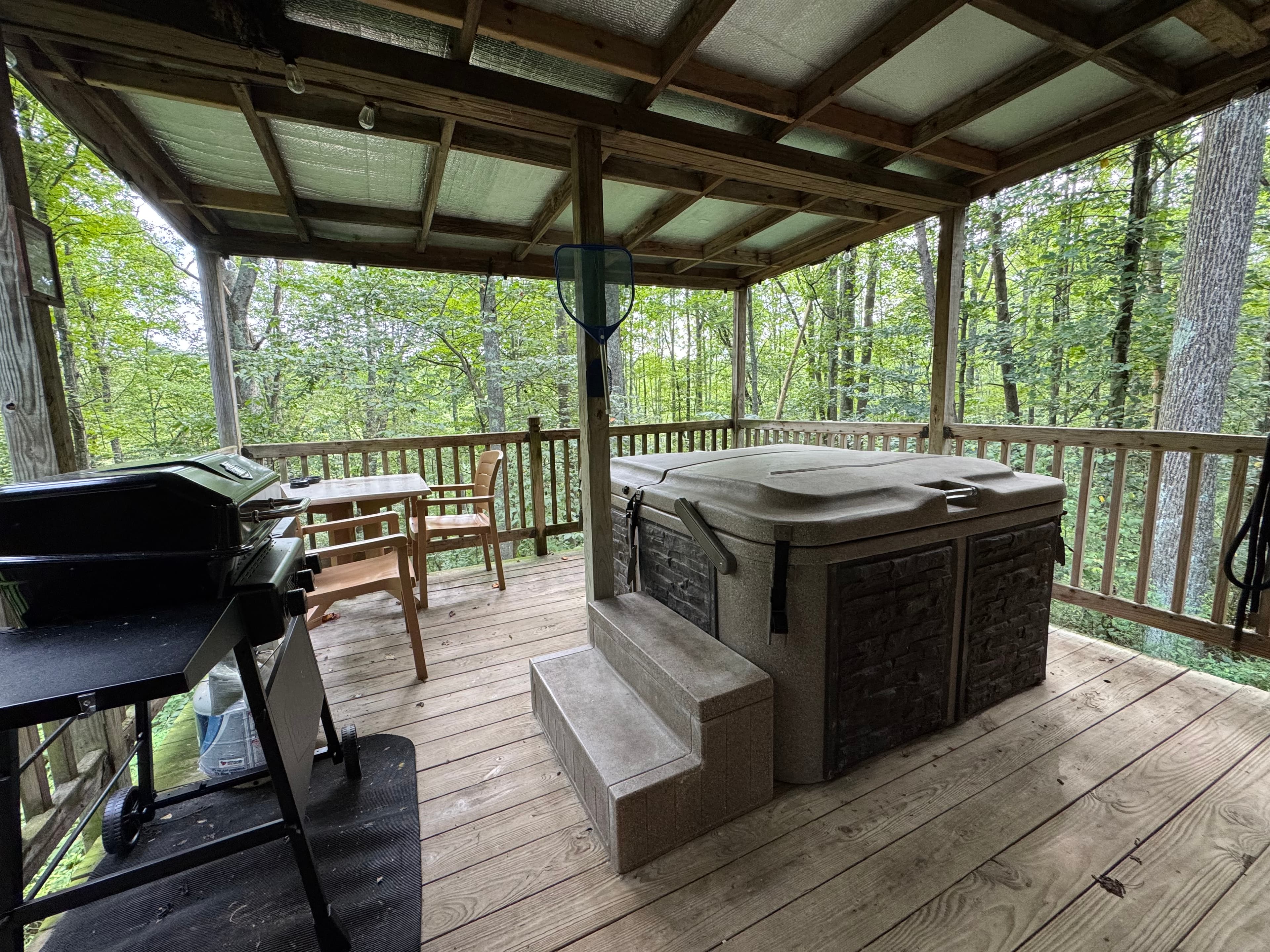A hot tub on a wooden deck surrounded by lush greenery.