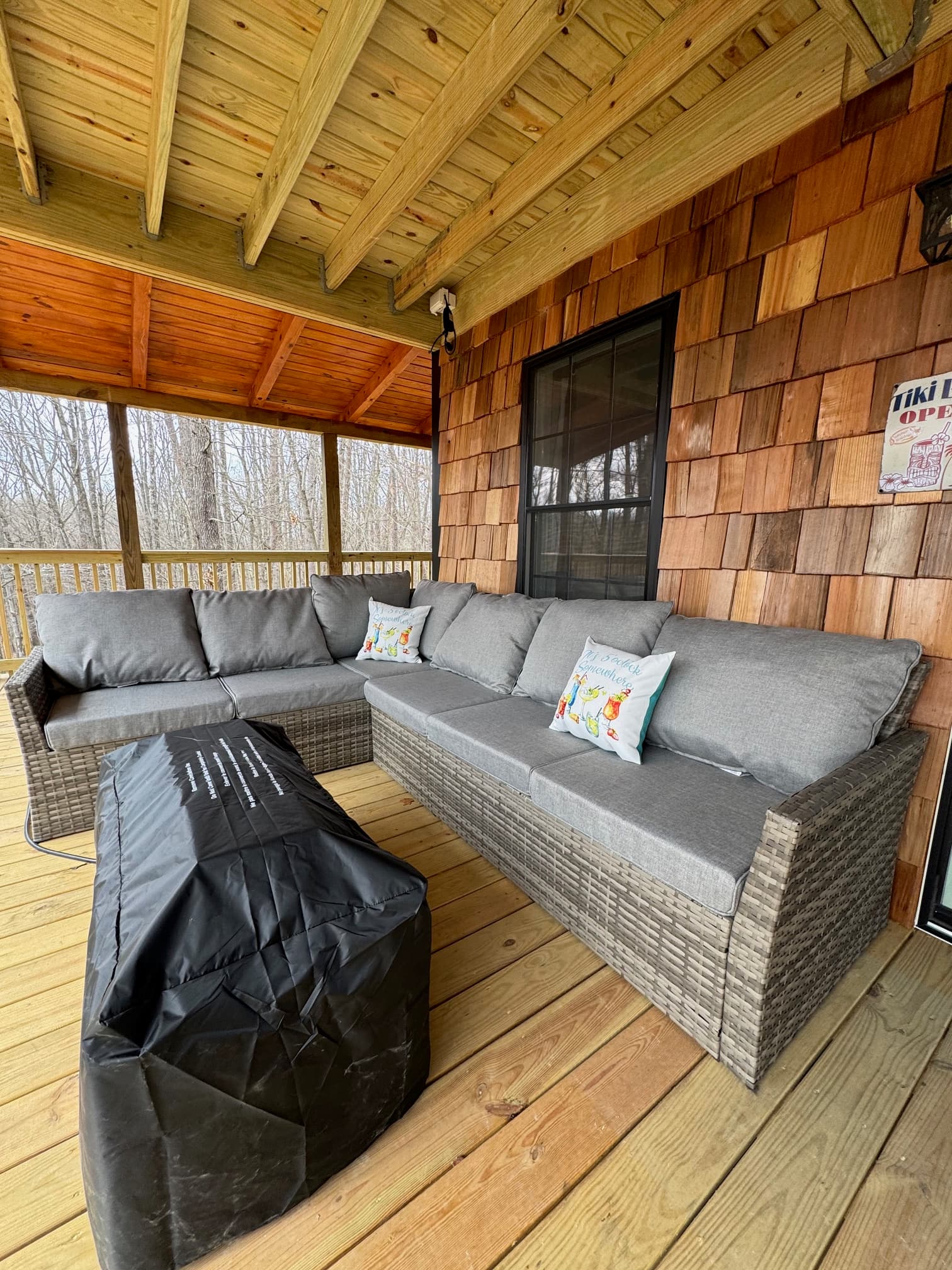 A gray cushioned outdoor sofa set with a black coffee table on a wooden porch.