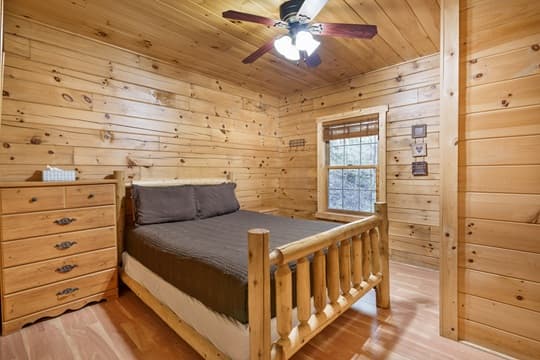 A cozy wooden bedroom featuring a log-style bed, dresser, and a ceiling fan.