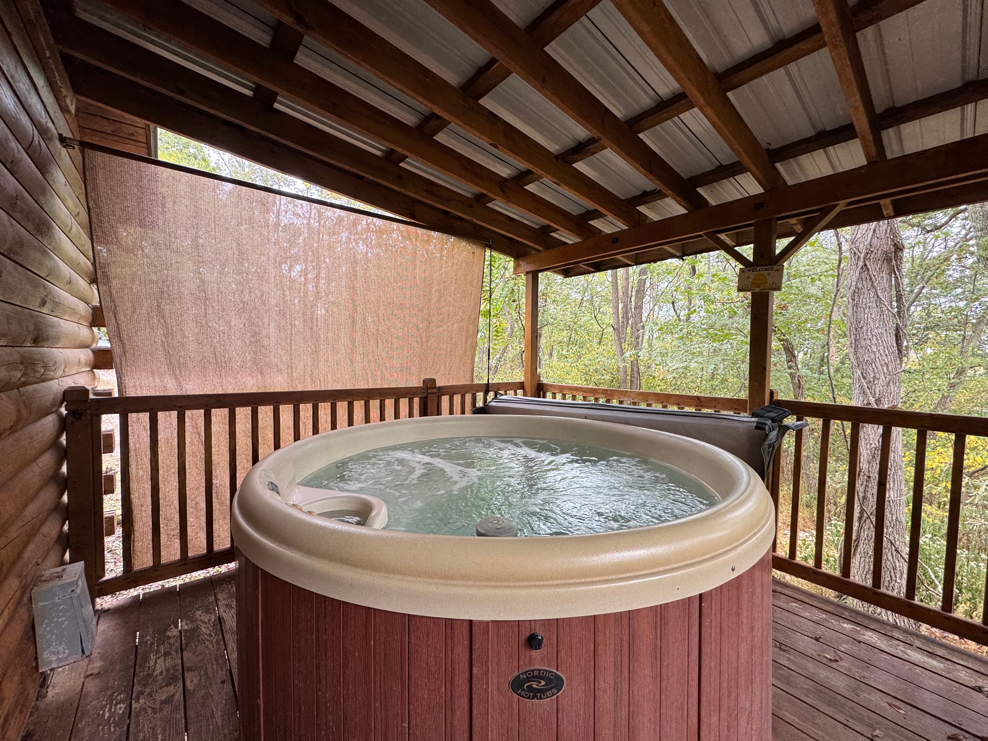 A wooden hot tub is set on a covered porch overlooking a forested area.