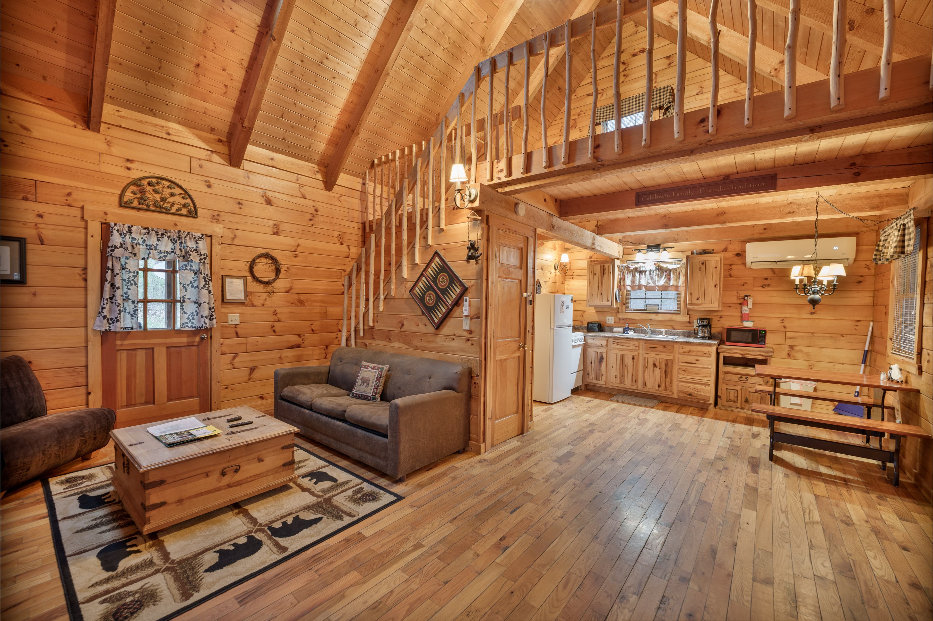 Cozy wooden cabin interior with vaulted ceilings, a sofa, and a kitchen area.