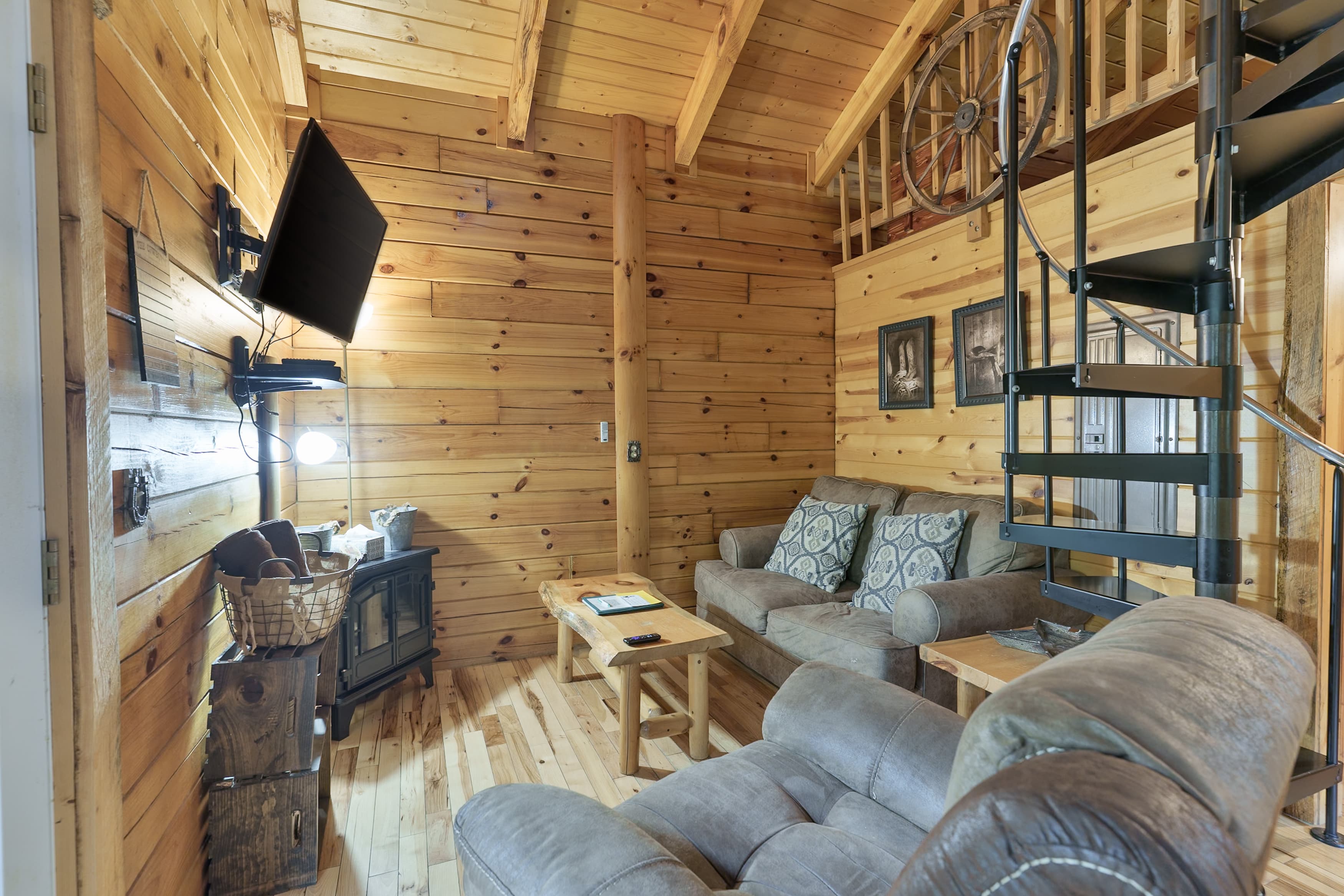 Cozy wooden cabin interior featuring a seating area, TV, and spiral staircase.