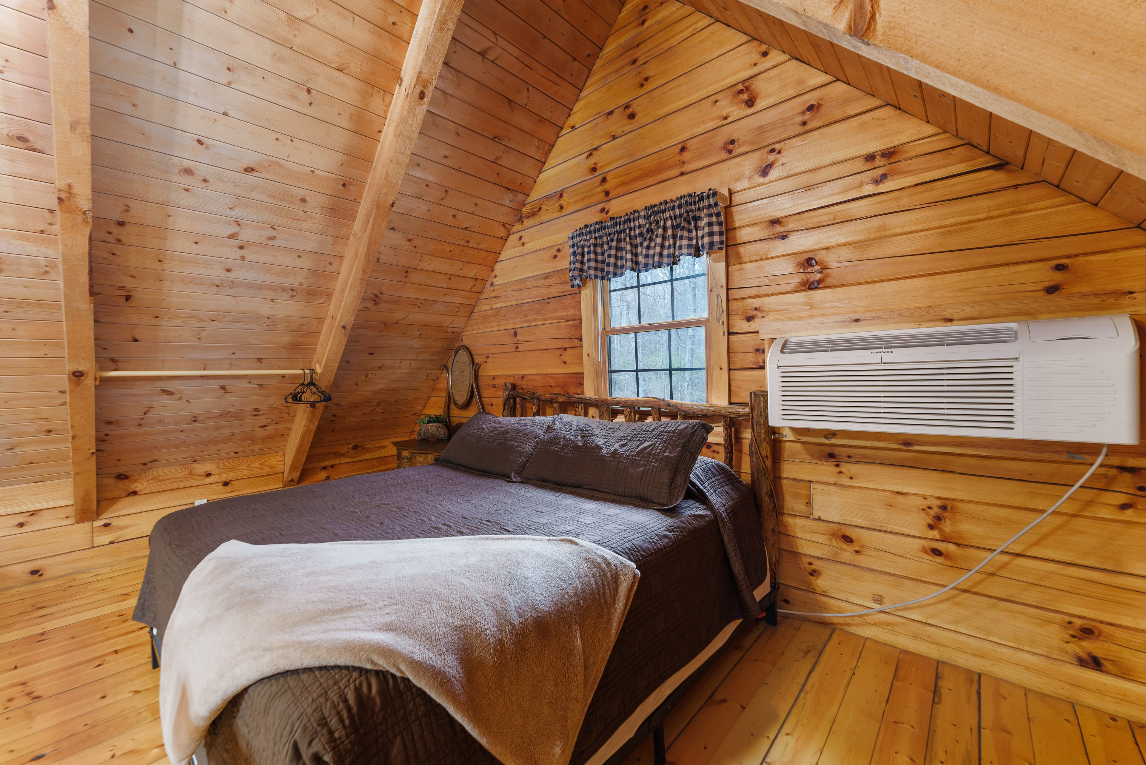 Cozy wooden bedroom with a double bed, blanket, and air conditioning unit.