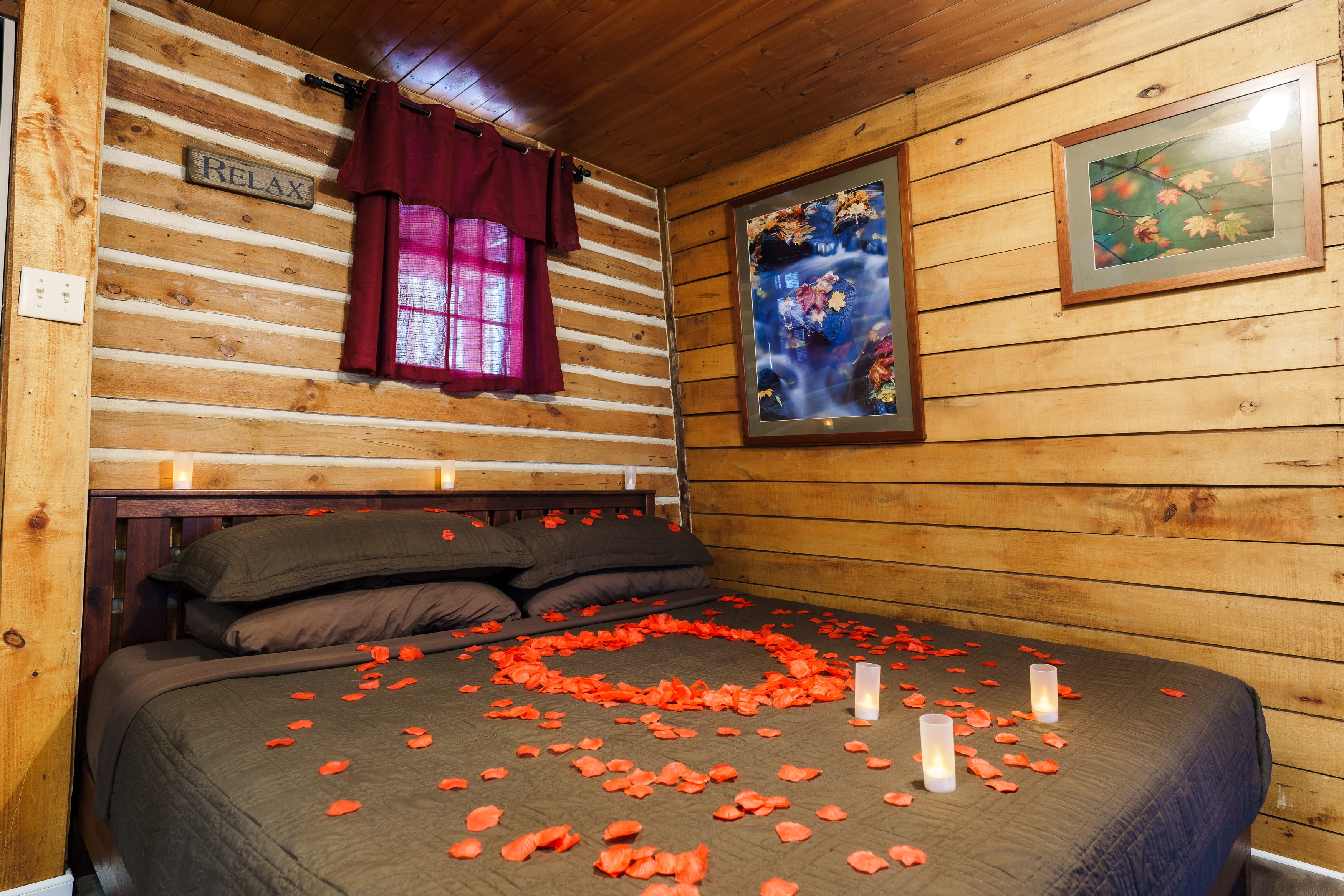 A cozy cabin bedroom featuring a bed adorned with rose petals and candles, inviting relaxation.