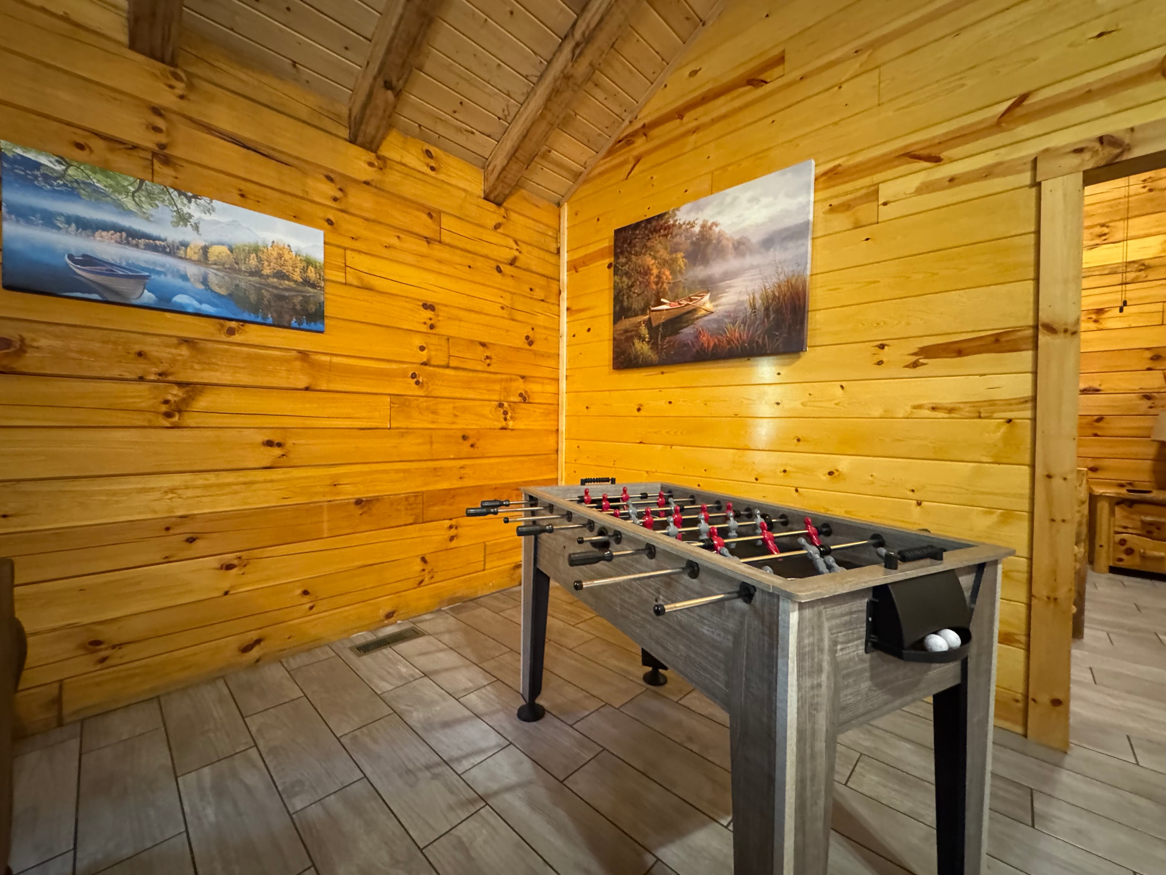 A foosball table is positioned in a cozy wooden room adorned with nature-themed paintings.