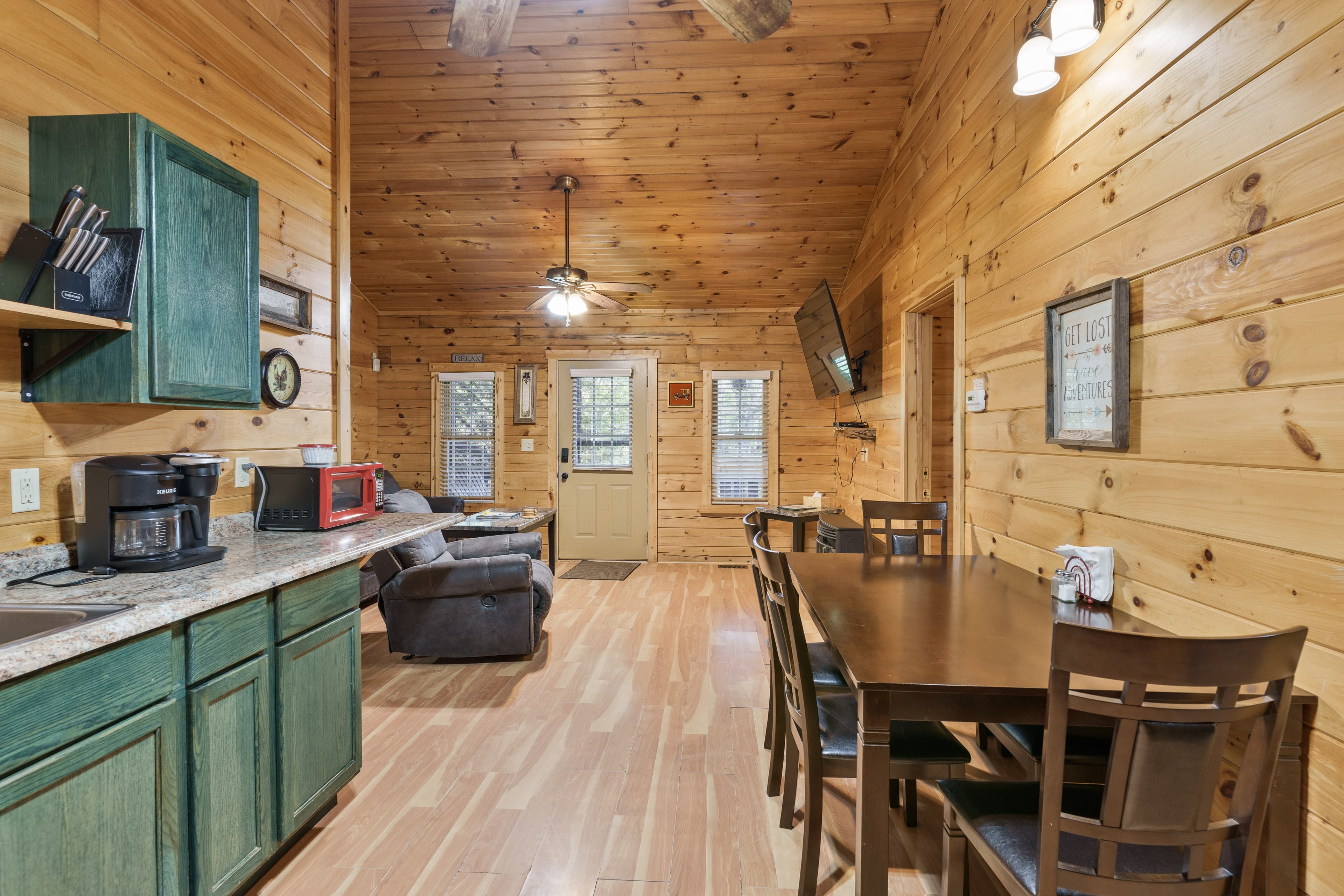A cozy kitchen and dining area featuring wooden walls, green cabinets, and a table with chairs.