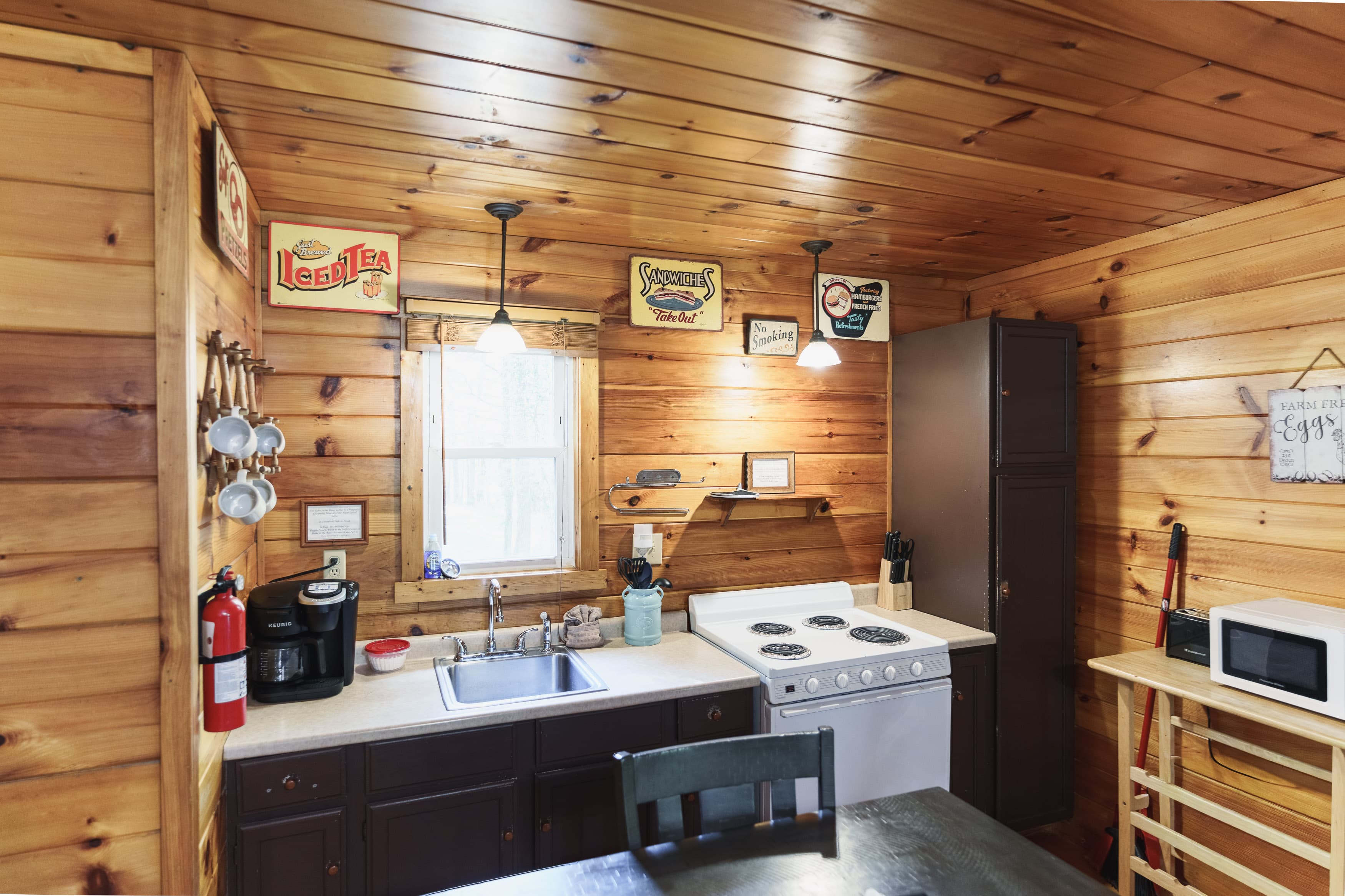 Cozy rustic kitchen with wooden walls, a sink, stove, and various kitchen accessories.