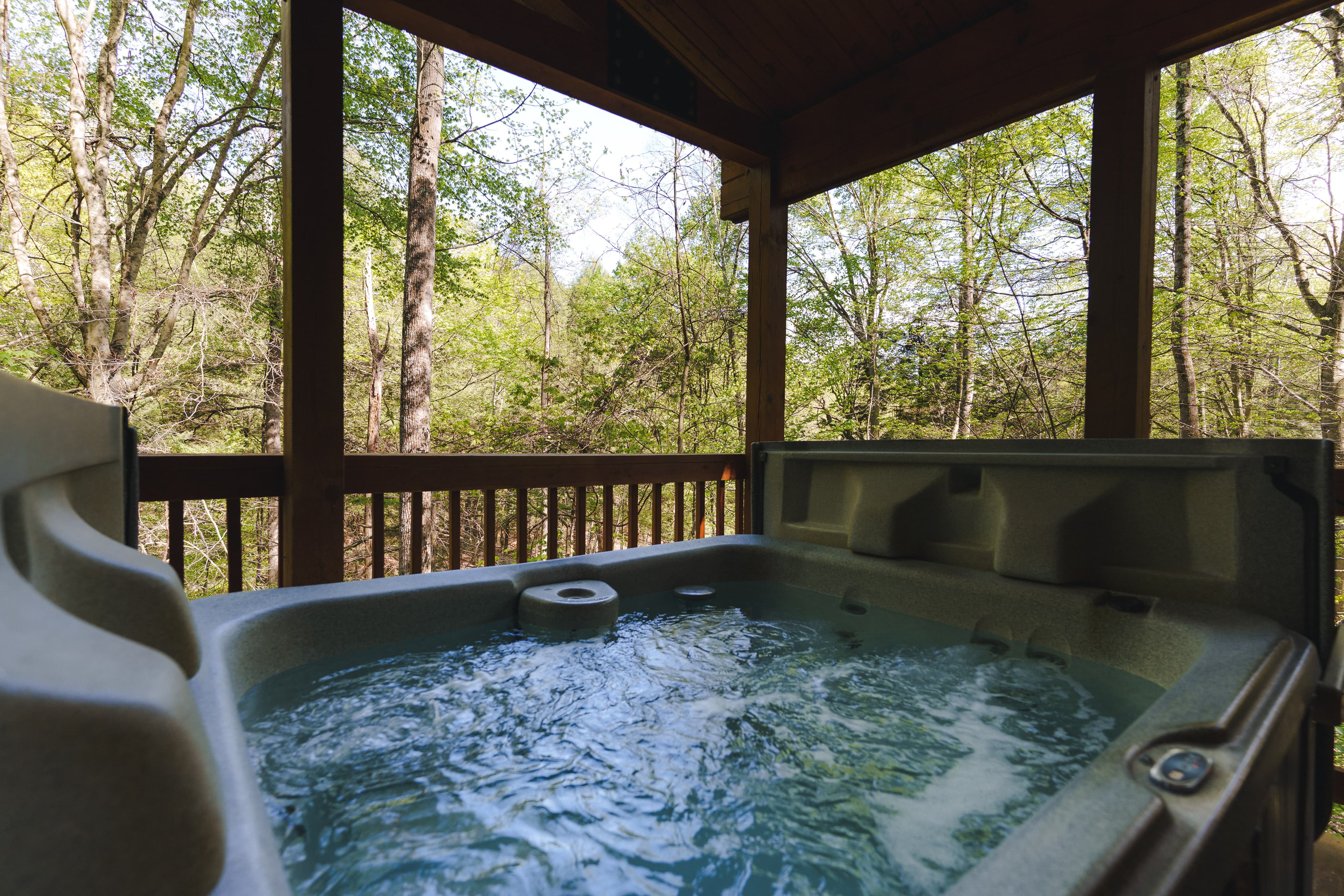 A hot tub on a porch overlooking a lush forest.