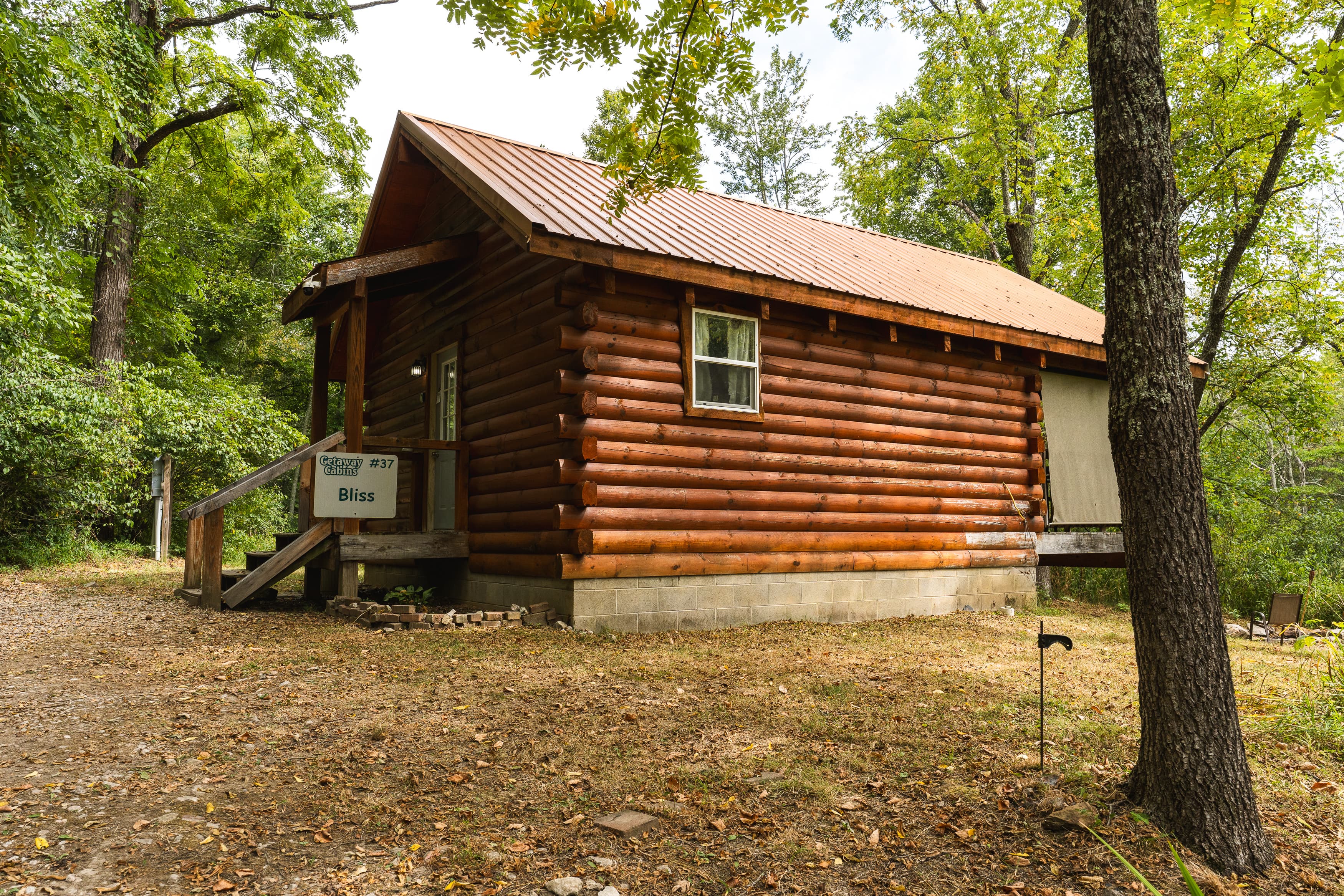 A rustic log cabin surrounded by trees and a grassy area.