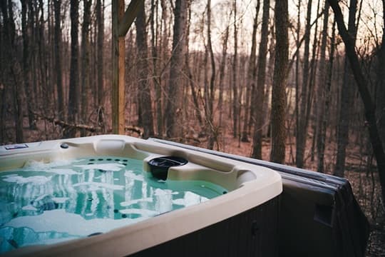 A hot tub sits on a deck overlooking a serene, wooded area at sunset.