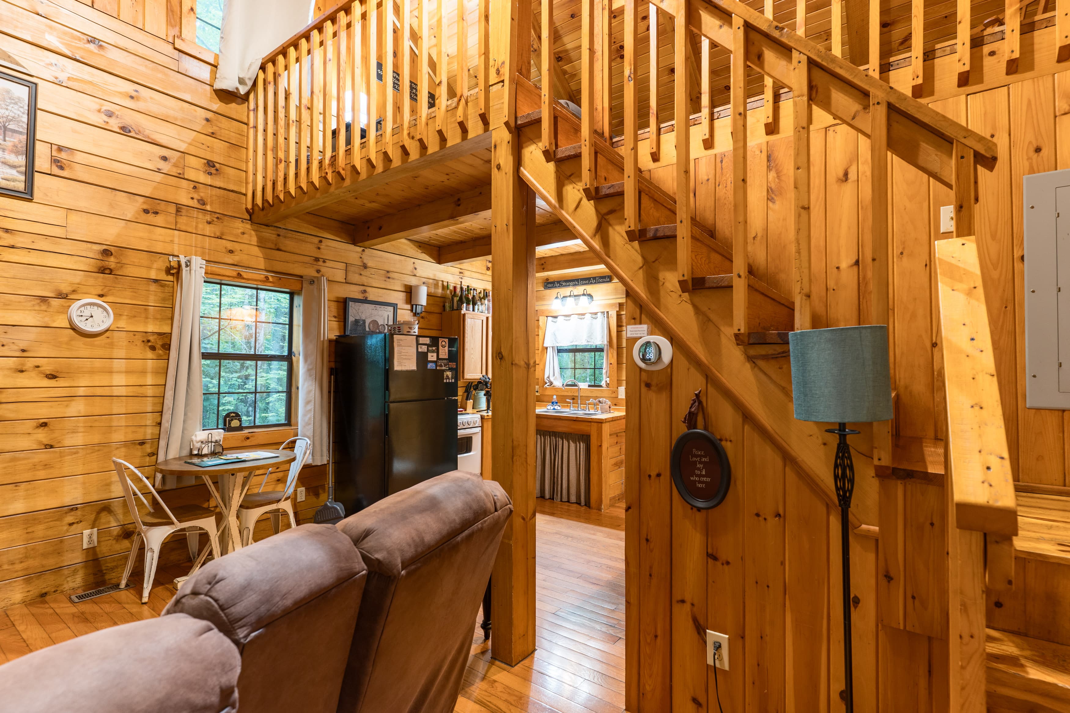 A cozy wooden interior of a cabin featuring a staircase, seating area, and kitchen.