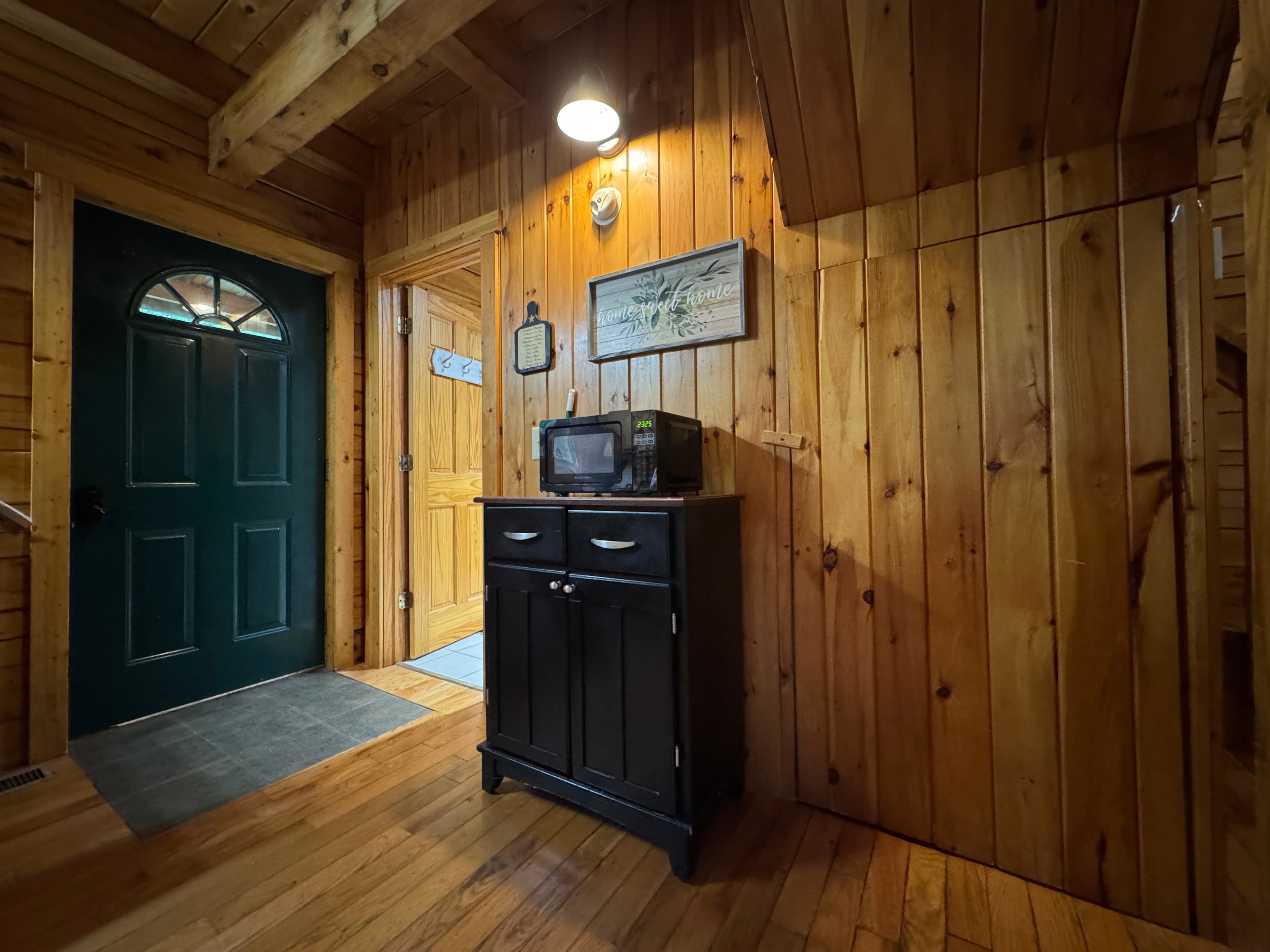 A cozy wooden hallway with a black cabinet, microwave, and a green front door.