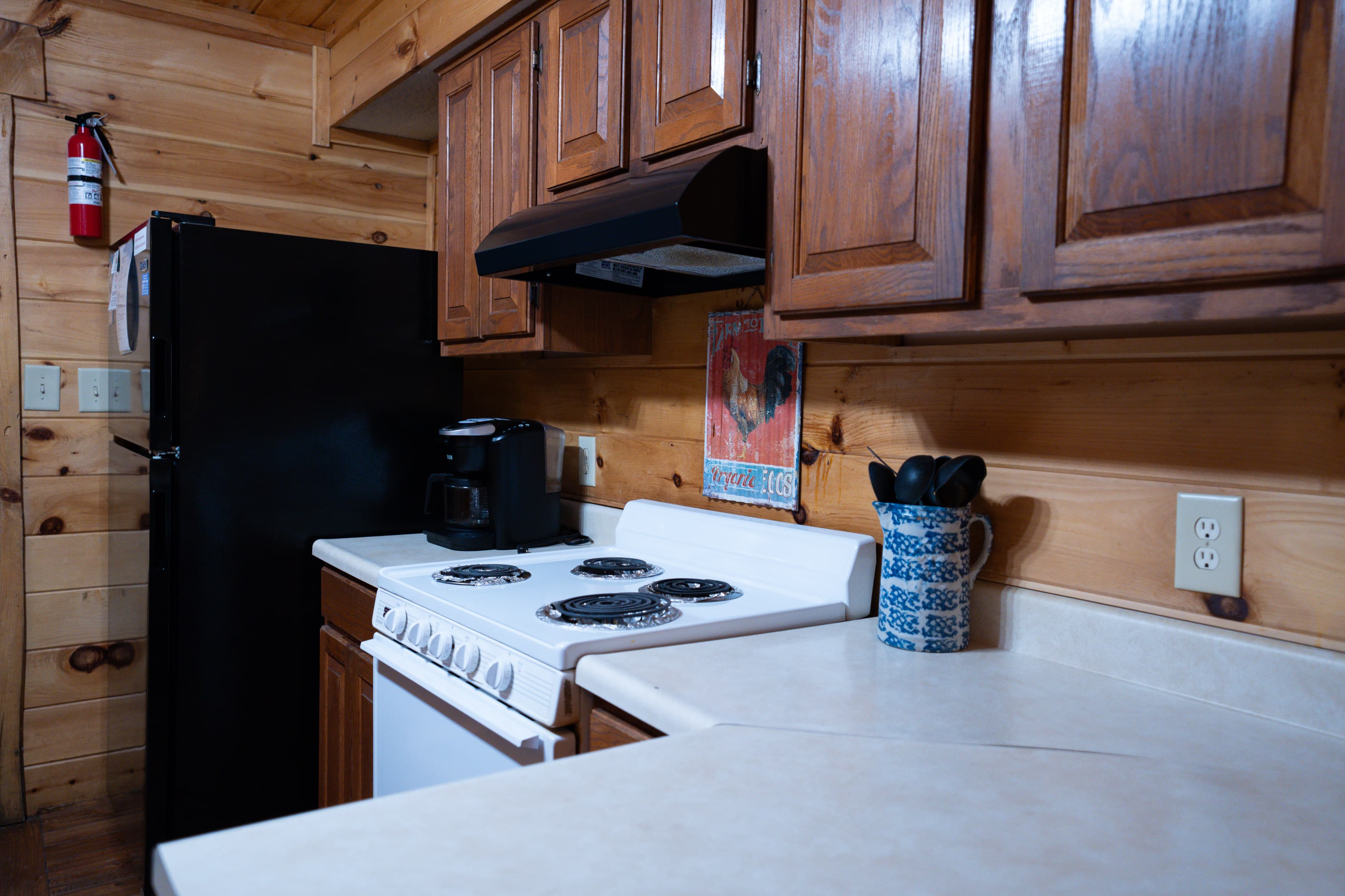 A rustic kitchen featuring wooden cabinets, a black refrigerator, and a white stove with a countertop workspace.